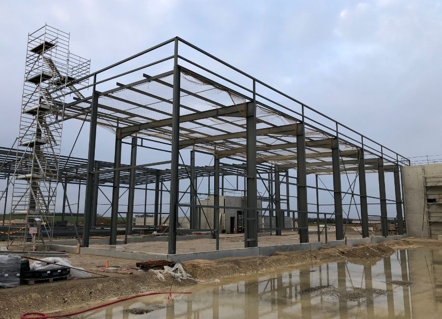 Vue latérale d’un hangar en construction avec sa structure métallique presque complète.