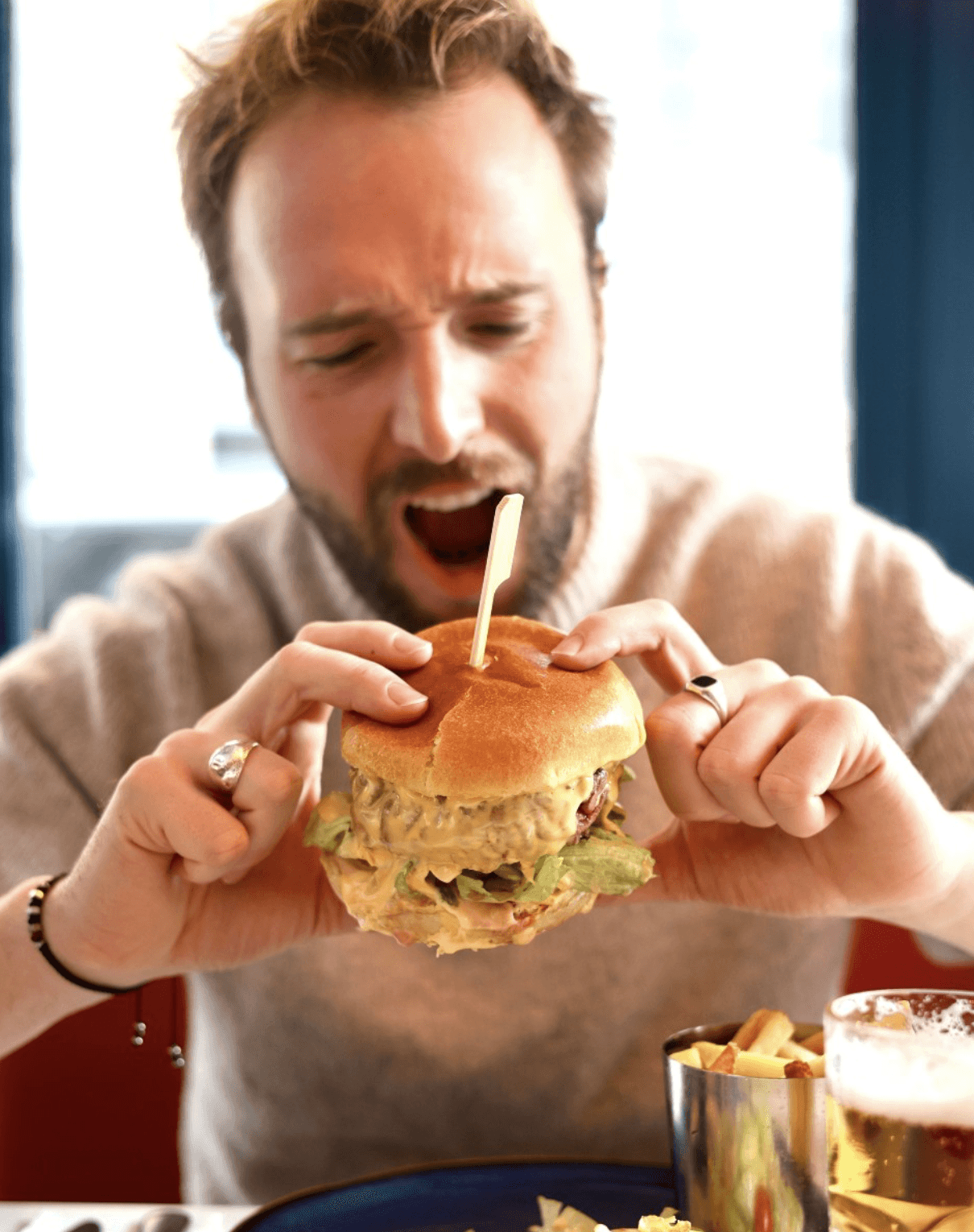 White plate with roasted carrots served on green sauce, topped with almonds and fresh herbs, held by a hand over a dark table.