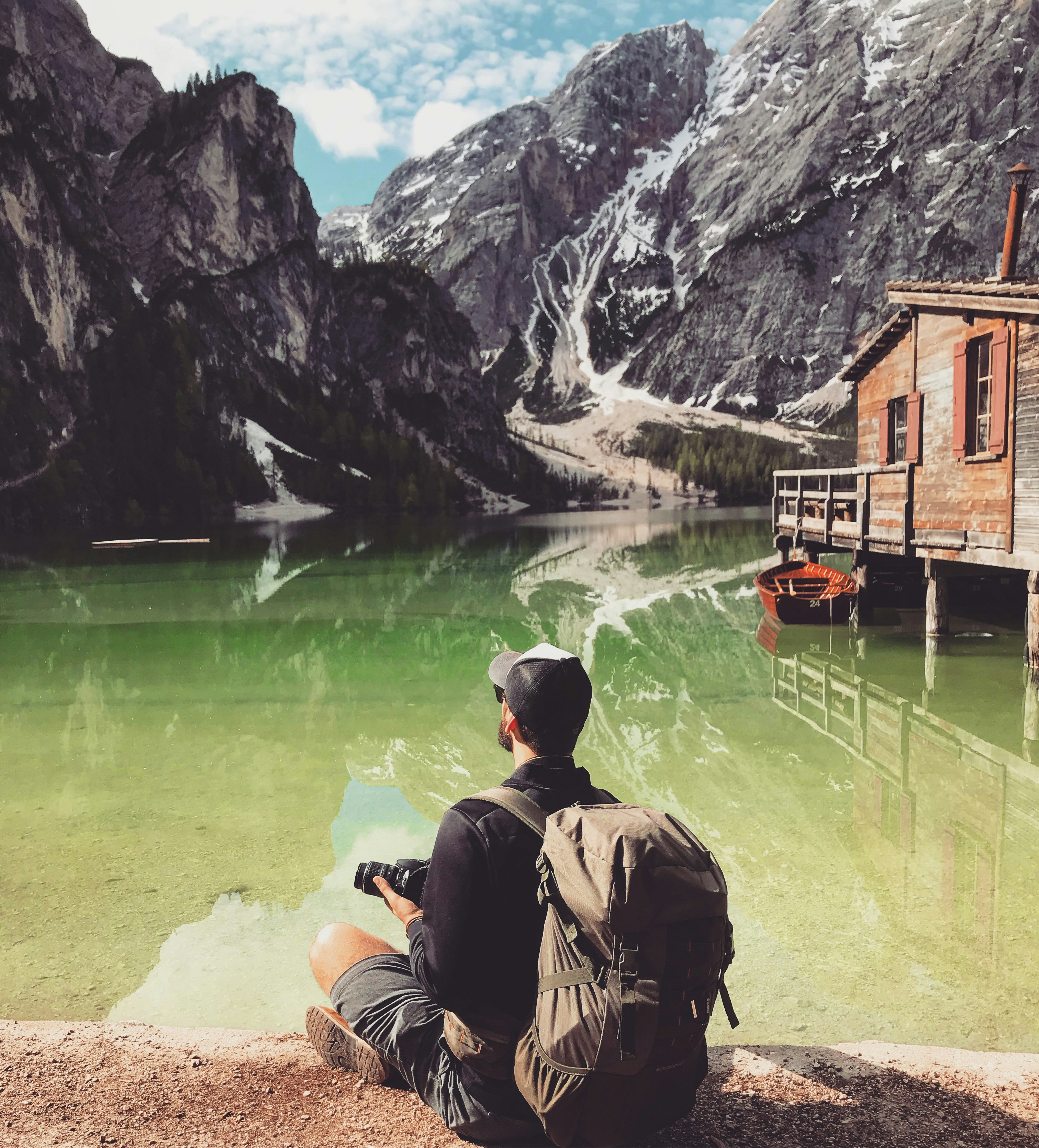 man in brown jacket sitting on brown rock near body of water during daytime