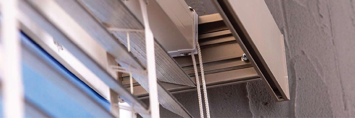 A person sits at a cluttered desk in a dimly lit room, focused on two monitors displaying aerial maps. The walls are covered with various images and notes.