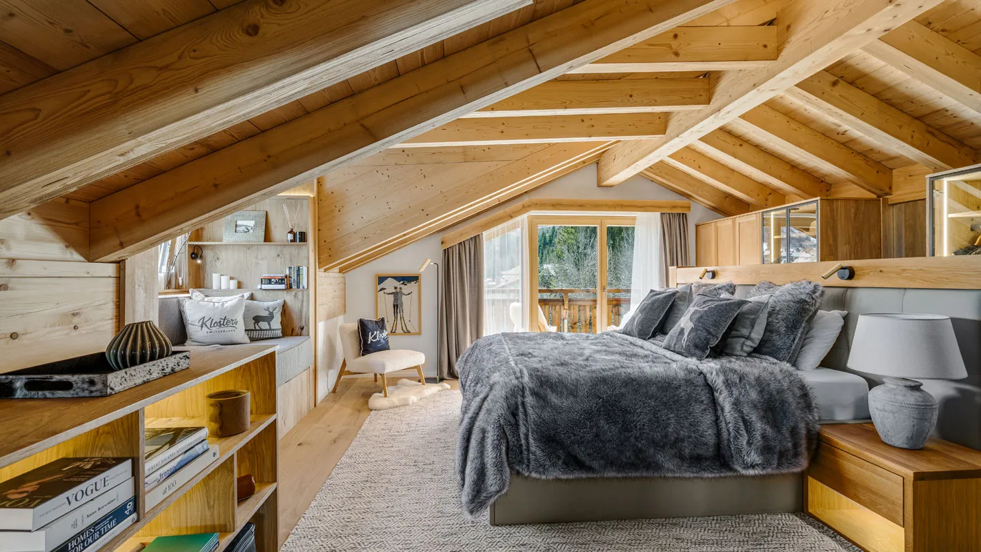 Silvretta Klosters master bedroom with exposed timber rafters, built-in shelving, and a view-facing bed
