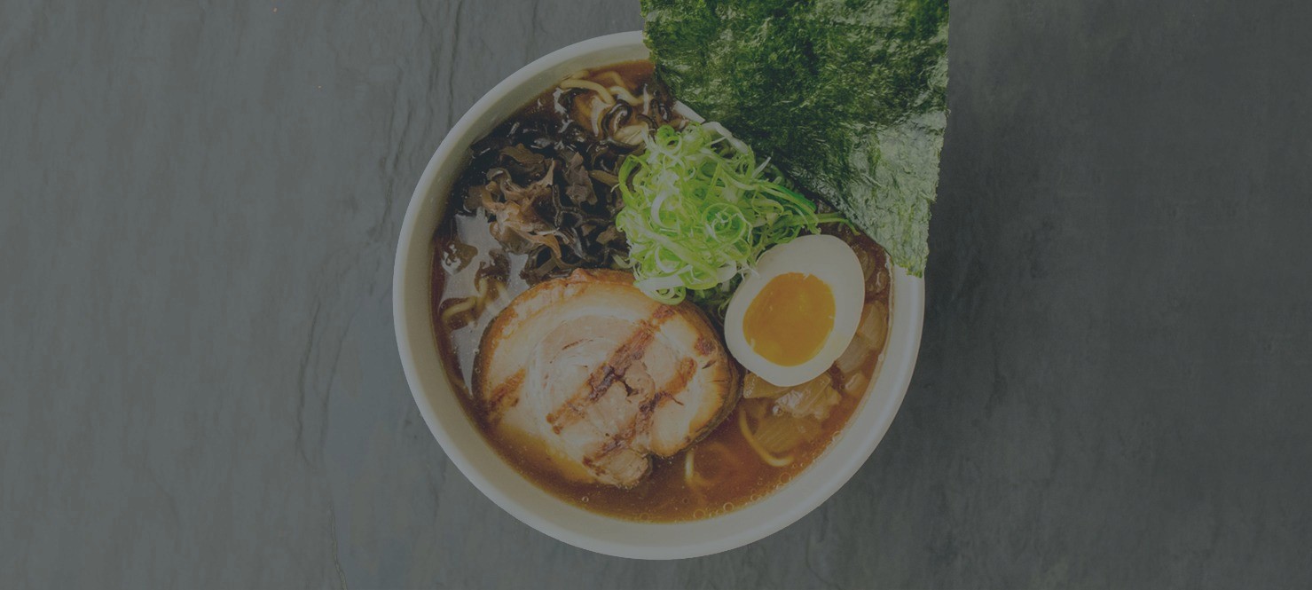 Toribashi ramen bowl with soft-boiled egg, mushrooms, and fresh herbs on a dark wood surface