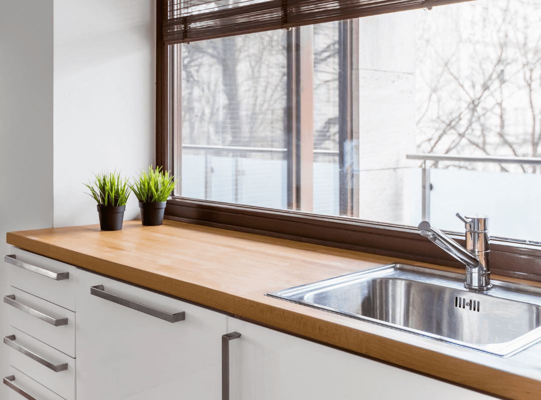 A kitchen with white millwork and butcher block countertops and a large bright window.