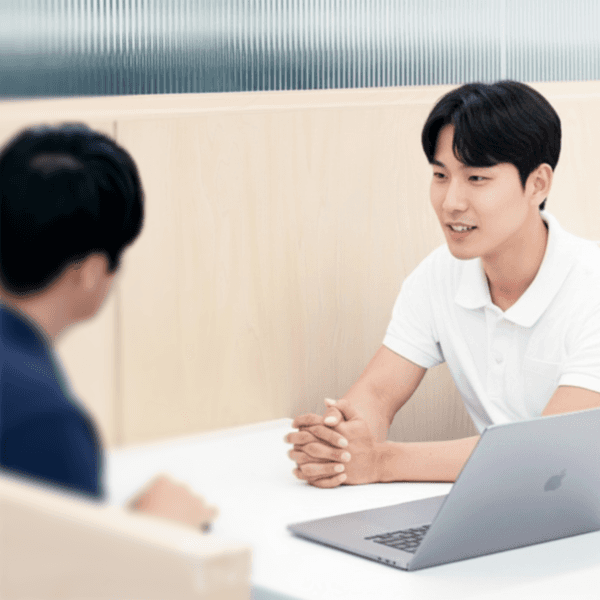 Two people are sitting at a table, engaged in conversation, with a laptop visible in front of them.