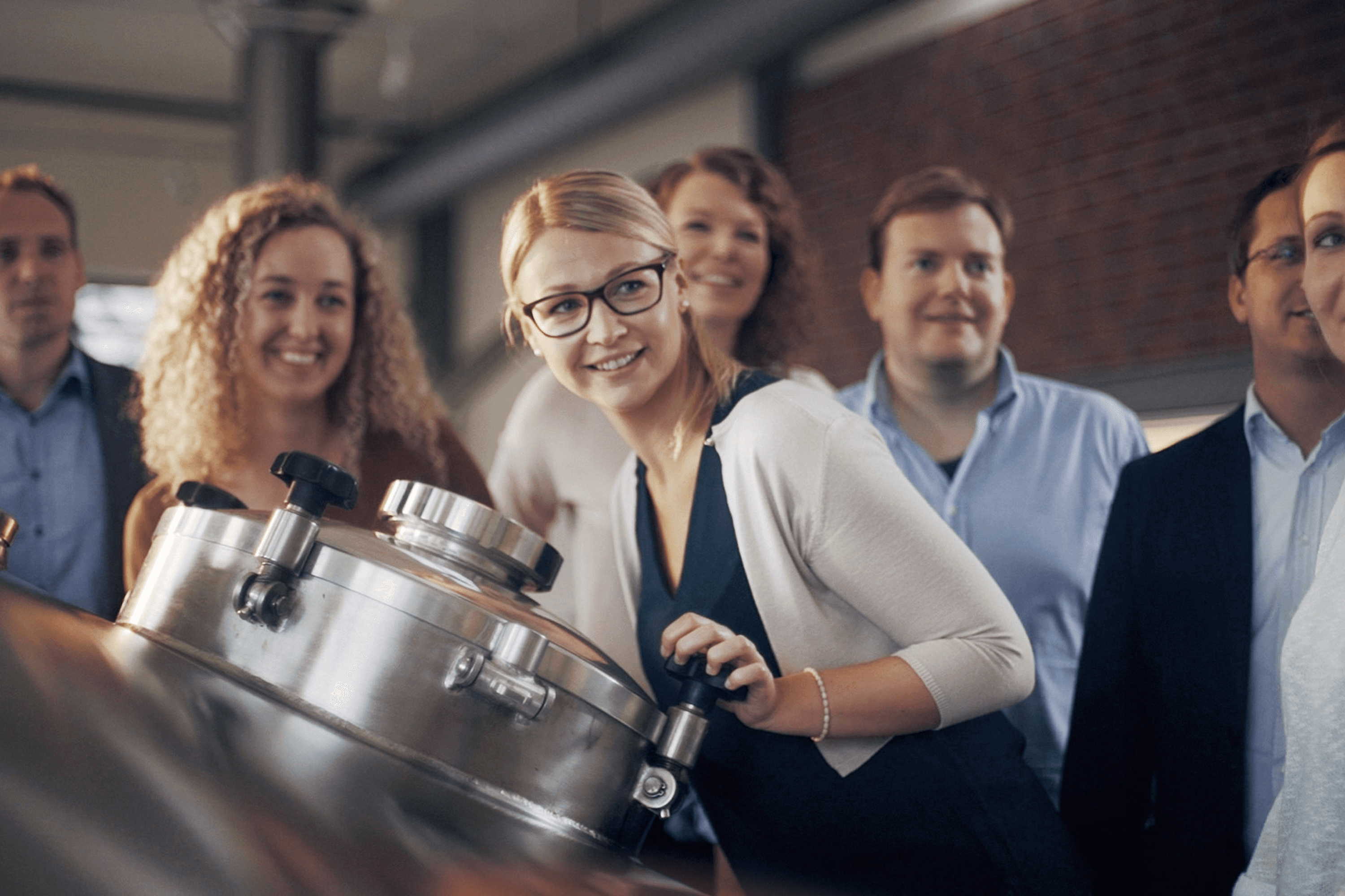People smiling near industrial brewing tank