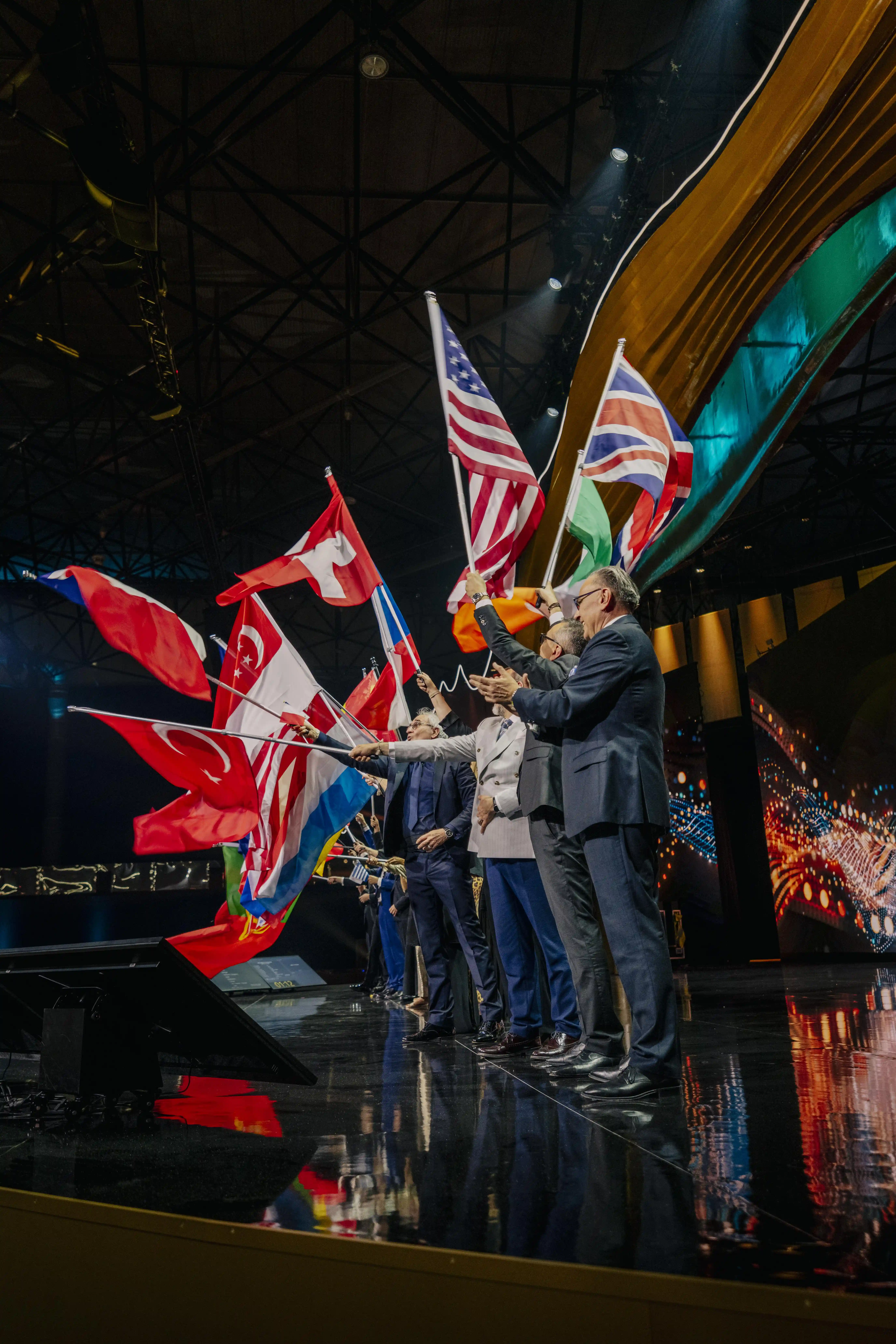 People waving international flags on the glossy stage under the golden wave canopy.