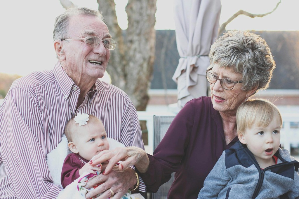 Two grandparents, smiling, holding their grandchildren