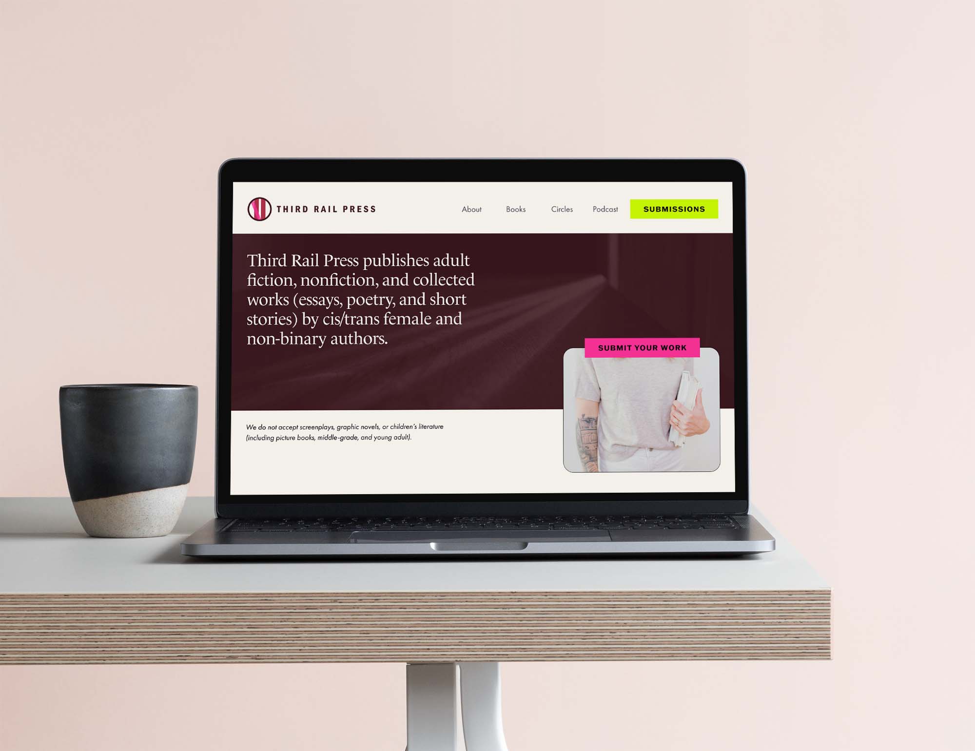 An open laptop sits on a simple wooden desk with a pottery mug sitting beside it, with a publishing company website on the screen