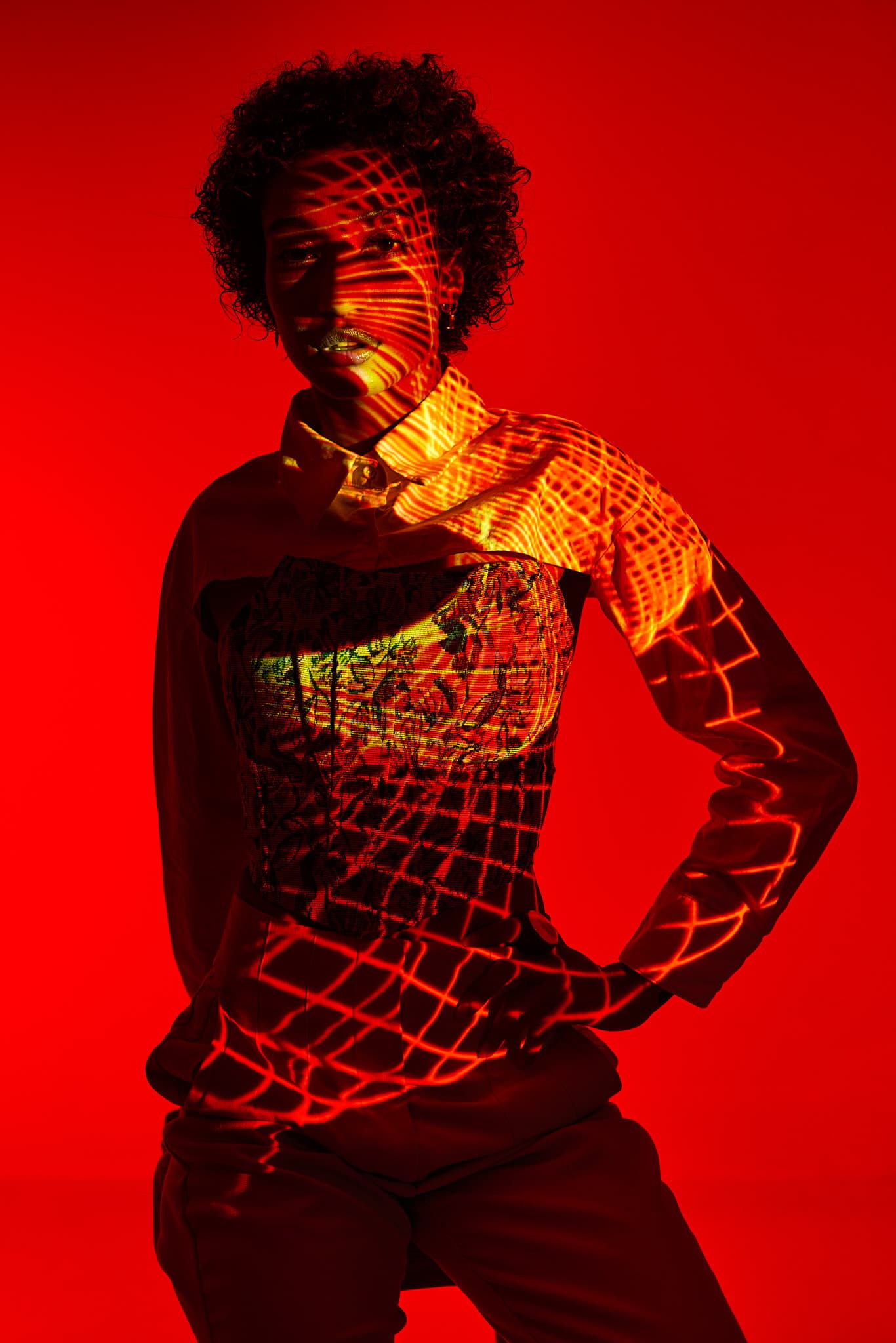 A model is illuminated with red lighting and geometric patterns projected onto her body in a photography studio.