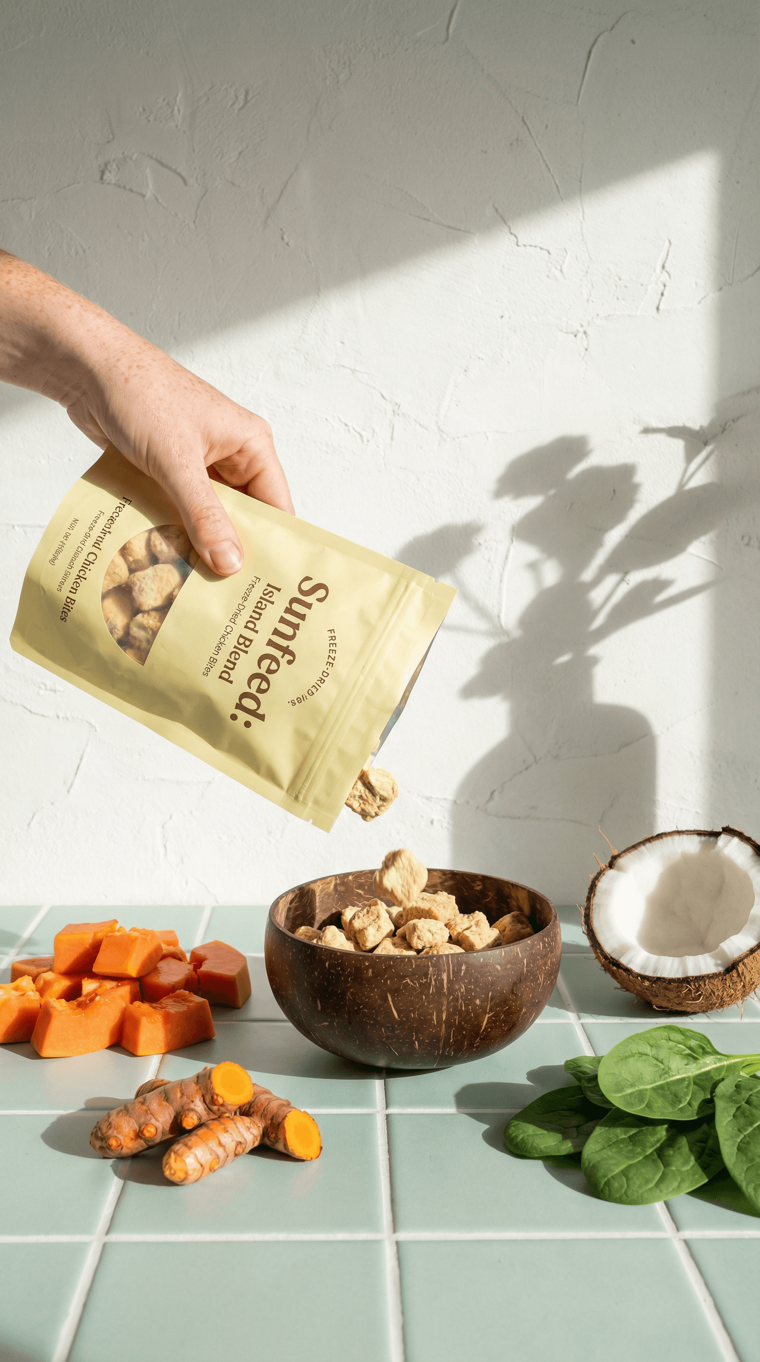 Hand pouring Sunfeed freeze-dried bites into a bowl with papaya, turmeric, coconut, and greens