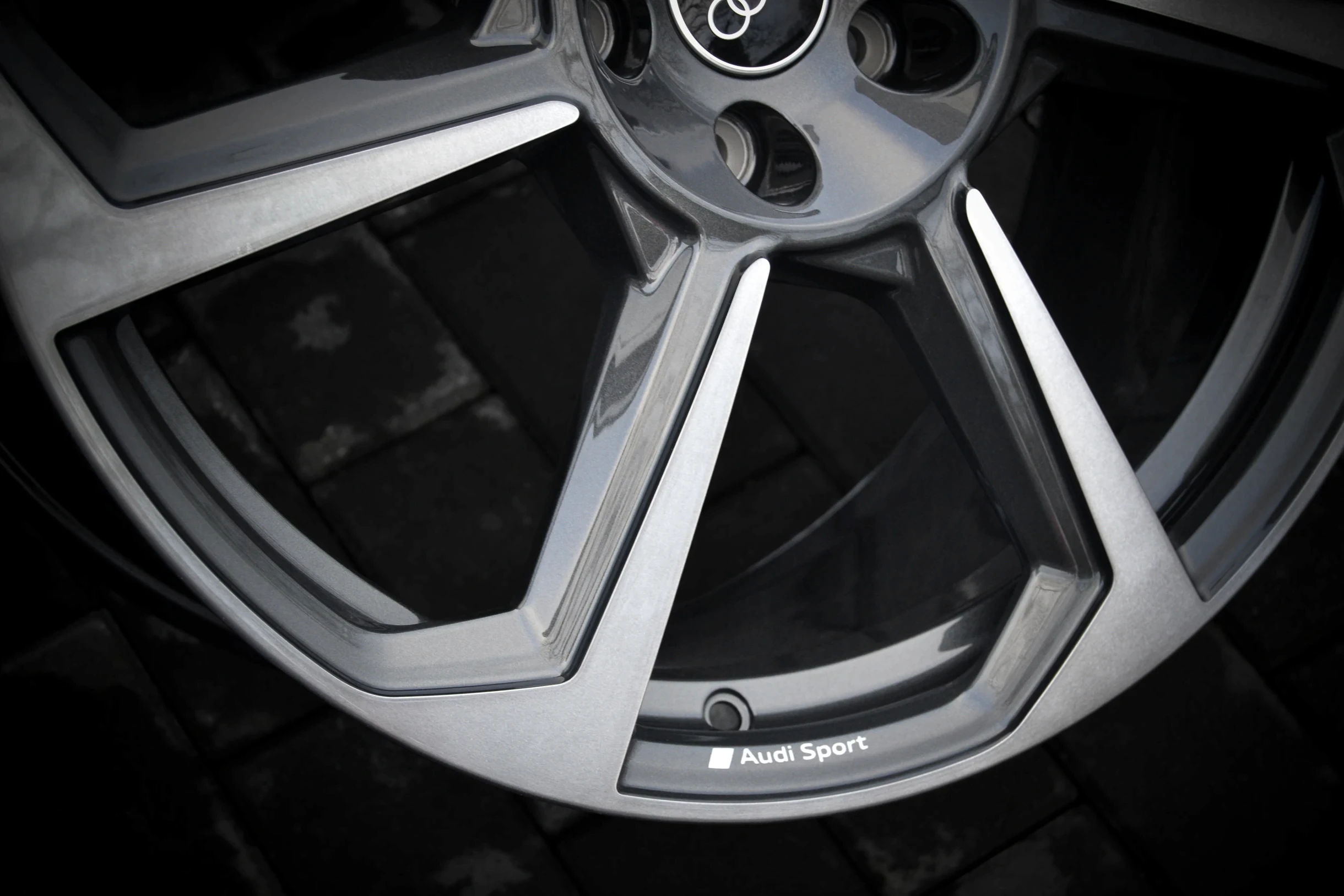 Nahaufnahme der silberfarbenen Speichenfront und des Audi-Sport-Schriftzugs am Felgenrand bei AT Plus.