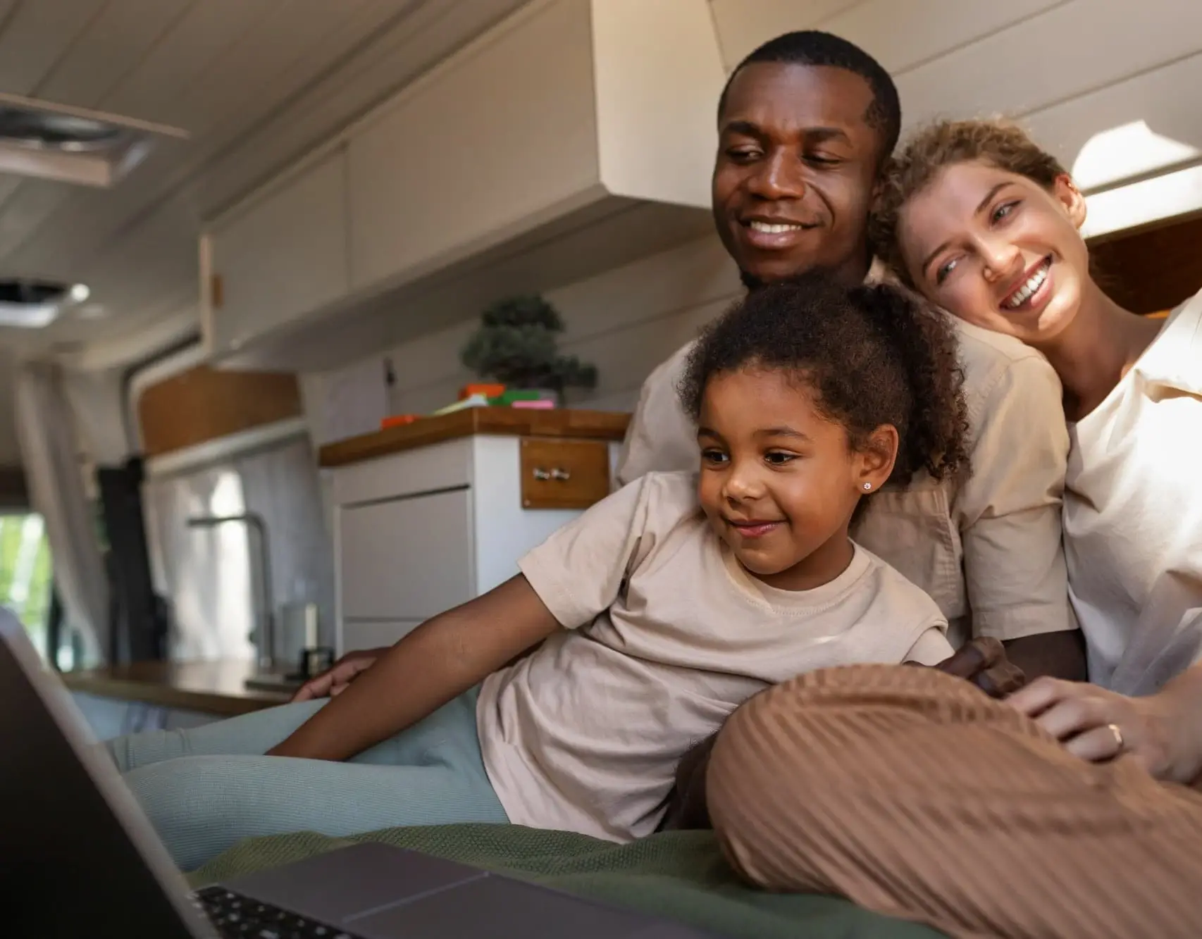 A smiling family relaxes together in their home, looking at a laptop. The warm light and cozy atmosphere represent comfort and financial peace of mind achieved through refinancing with Chris Lewis Home Loans.