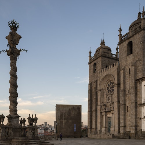 Historic stone cathedral with ornate spires, a twisted column, and a small figure in the foreground under a clear sky.