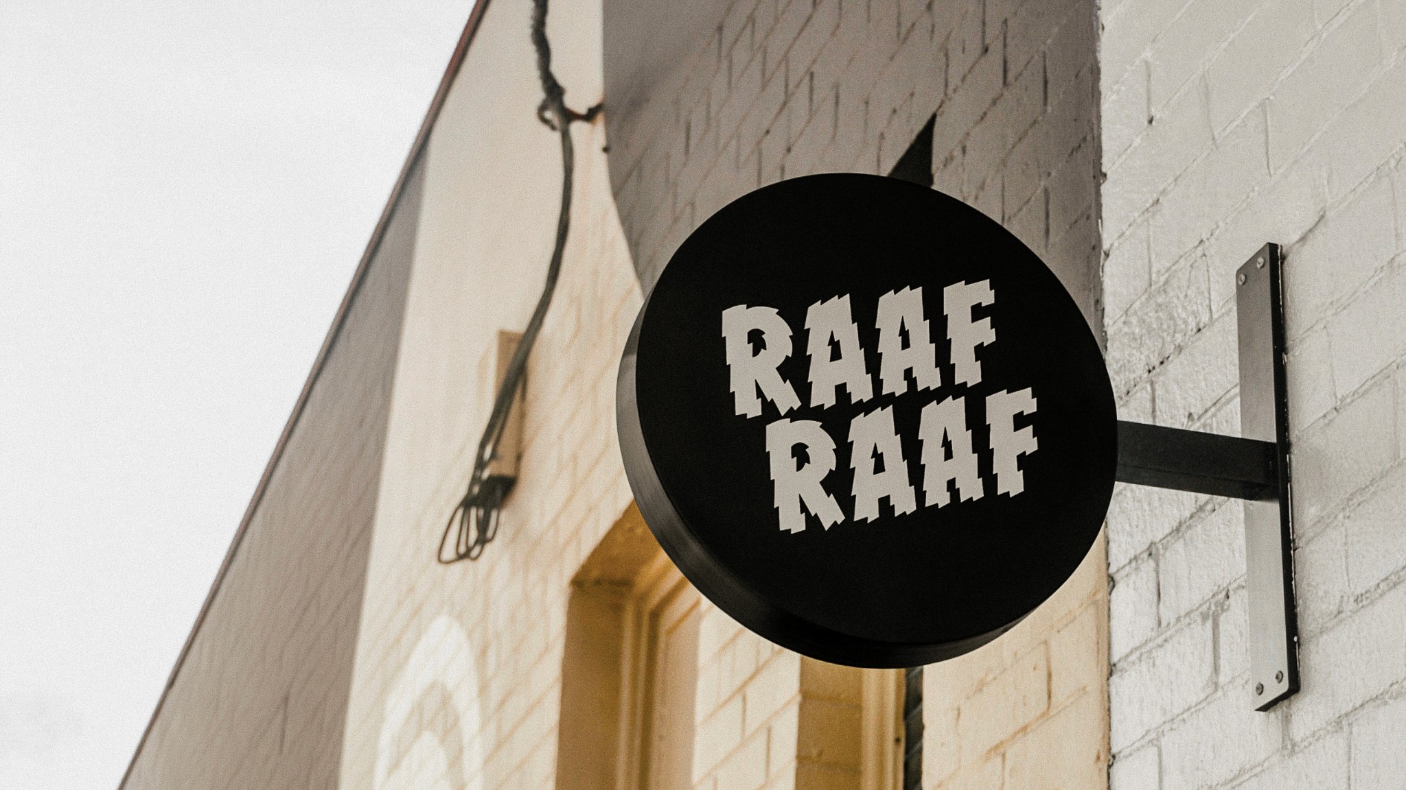 A person stands against a vibrant background of orange and yellow wavy patterns. They are wearing a dark coat, looking contemplative and thoughtful.