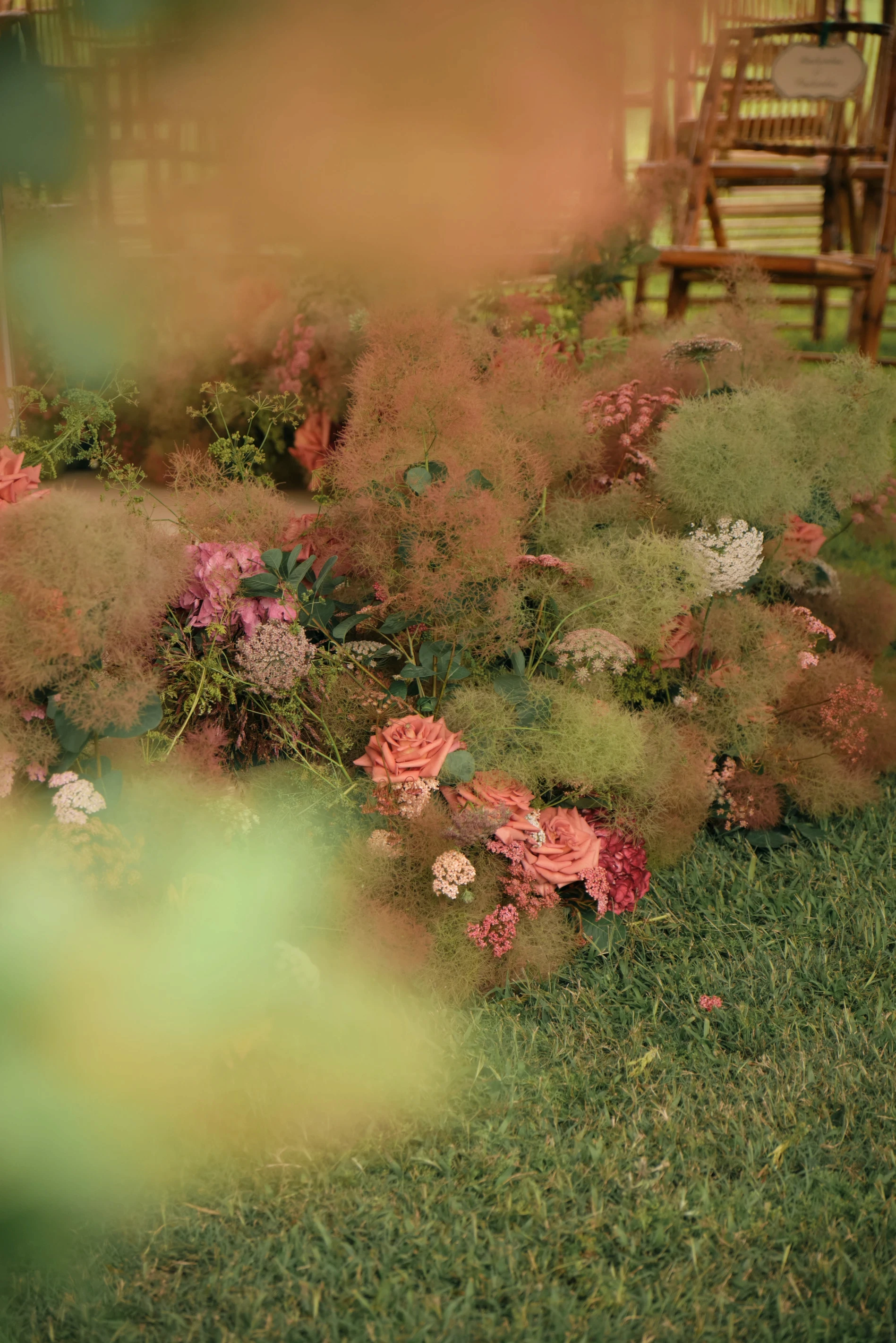 Primer plano desenfocado de flores etéreas y rosas en tonos tierra integradas en el césped.