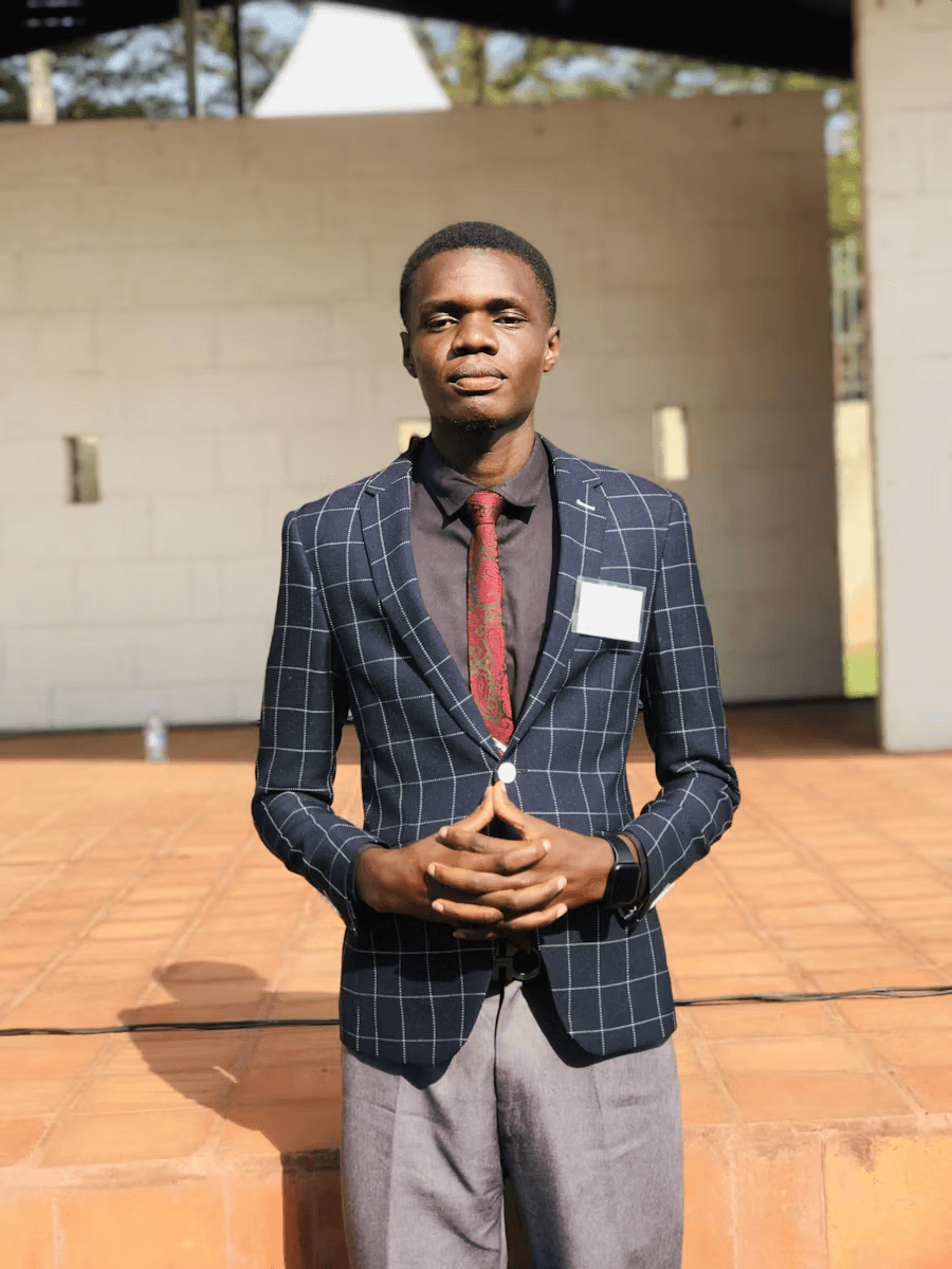 A high school student standing at a conference poster presentation, dressed professionally, holding printed research materials
