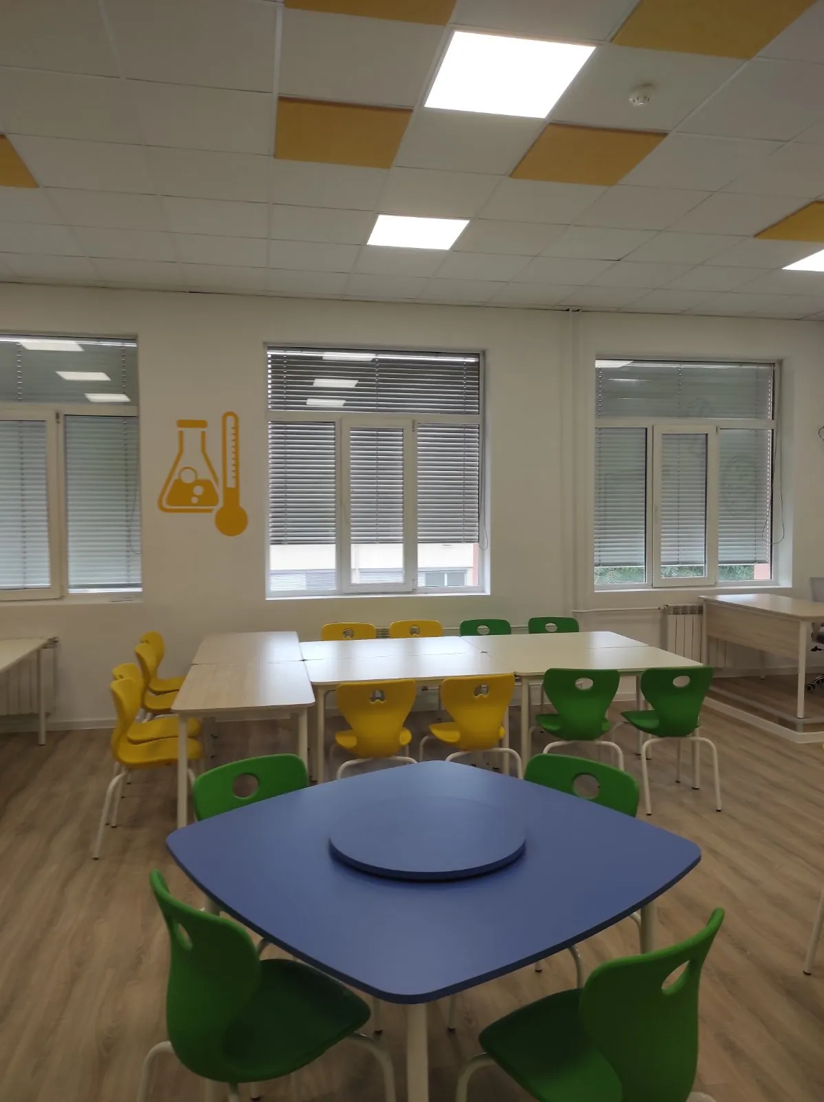 Green and yellow school chairs with blue classroom tables in a science room