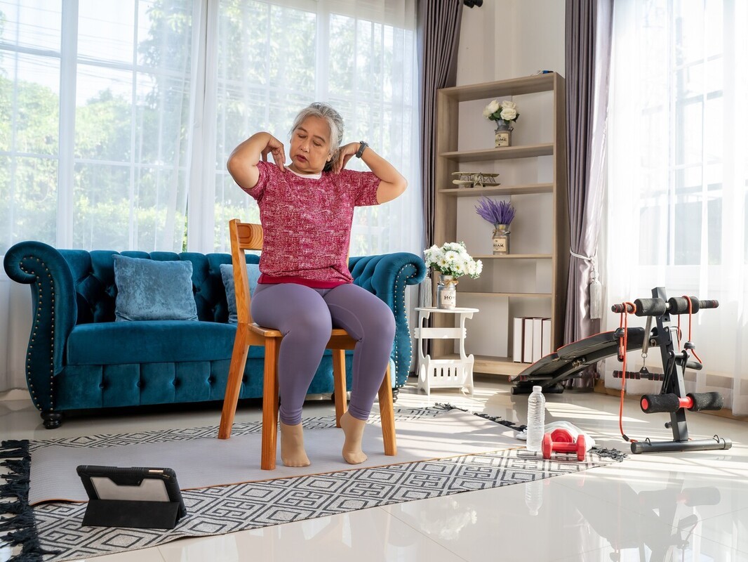 older woman following a routine of chair exercises for seniors to lose weight on her tablet