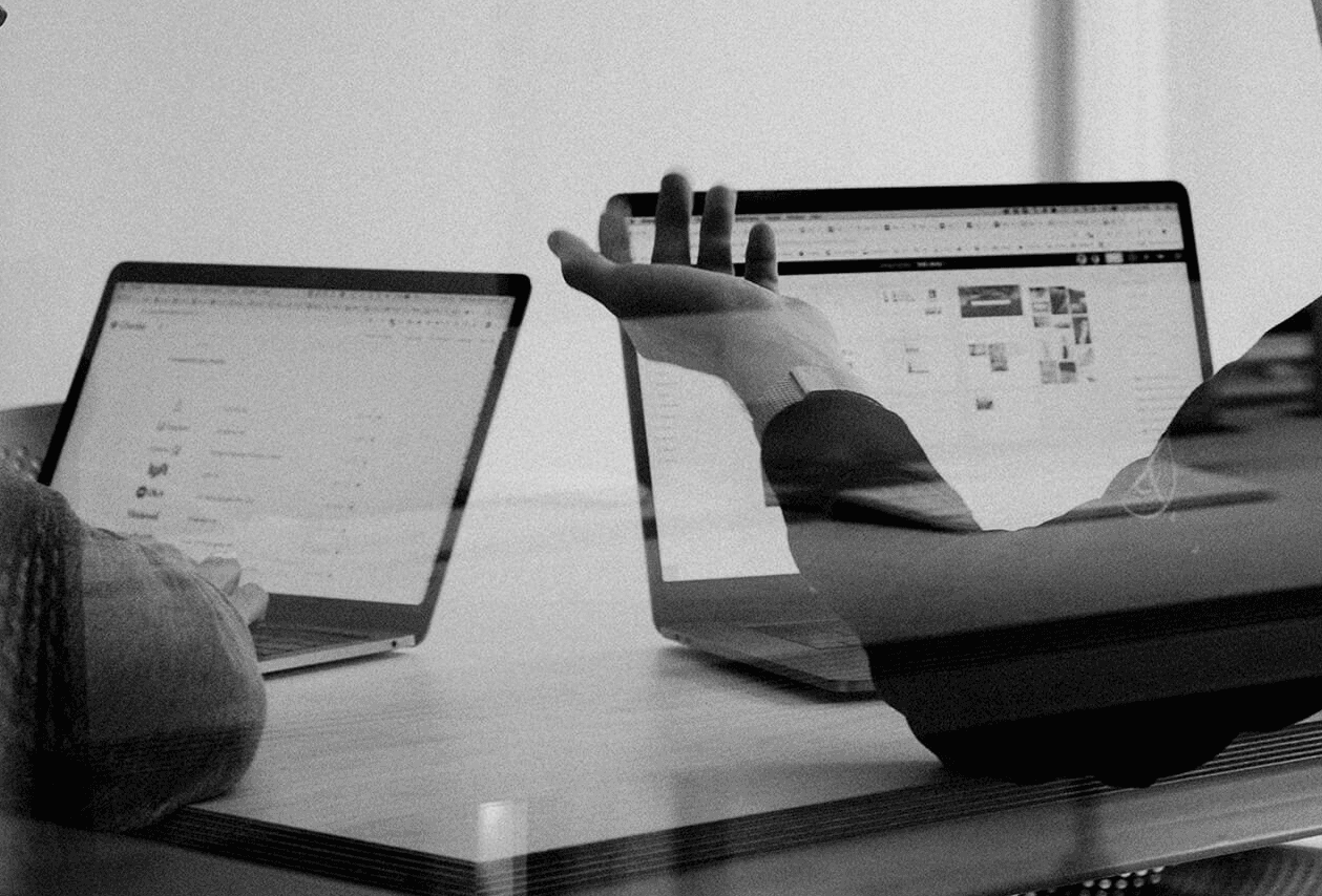 Black and white image of people working at a table with laptops, showing hands gesturing during discussion of digital content displayed on screens, with fabrica® logo in the corner.