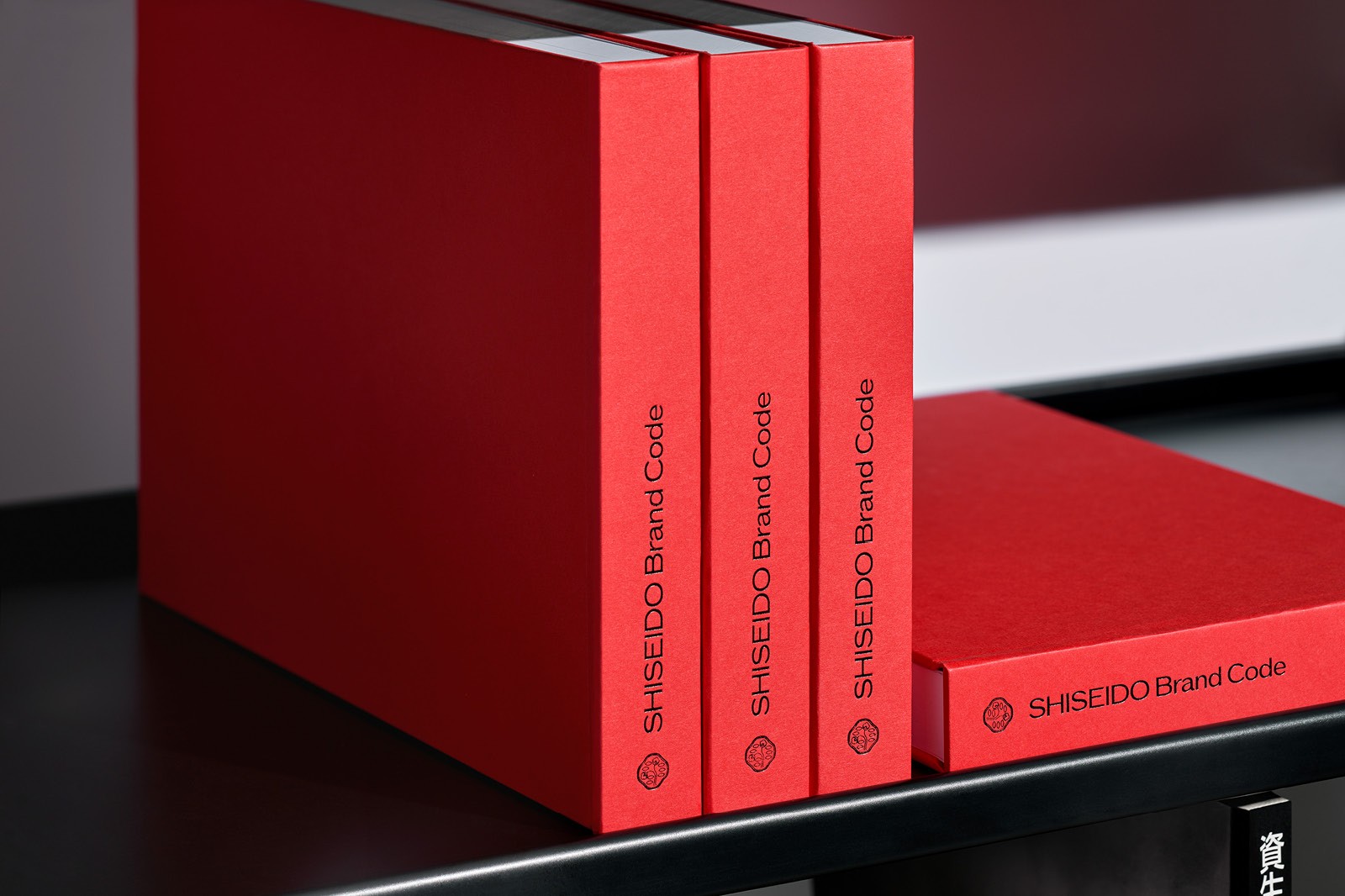 A stack of red books titled Shiseido Brand Code neatly arranged on a black shelf, showcasing their vibrant color and clean design.