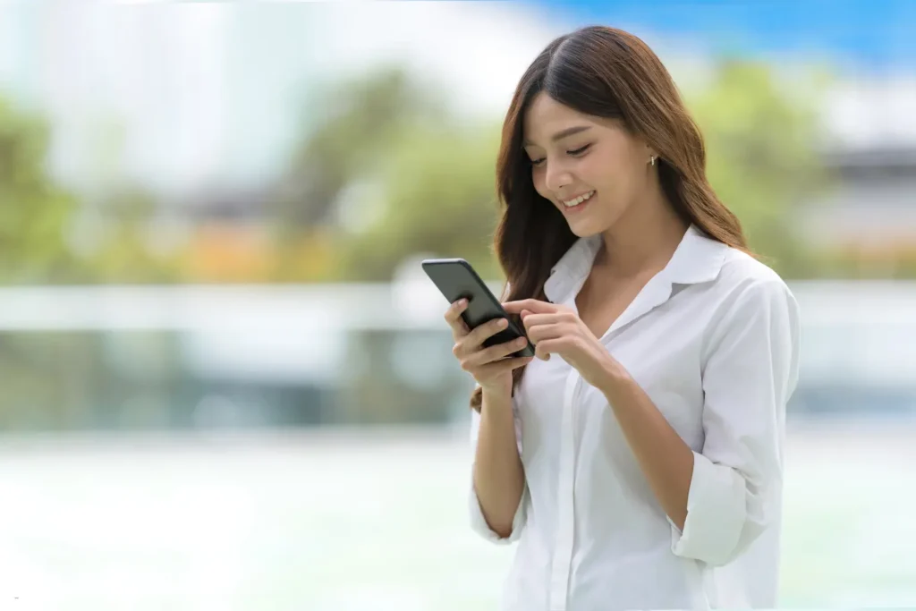 Landlord-tenant communication through smartphone app as woman smiles while messaging outdoors.