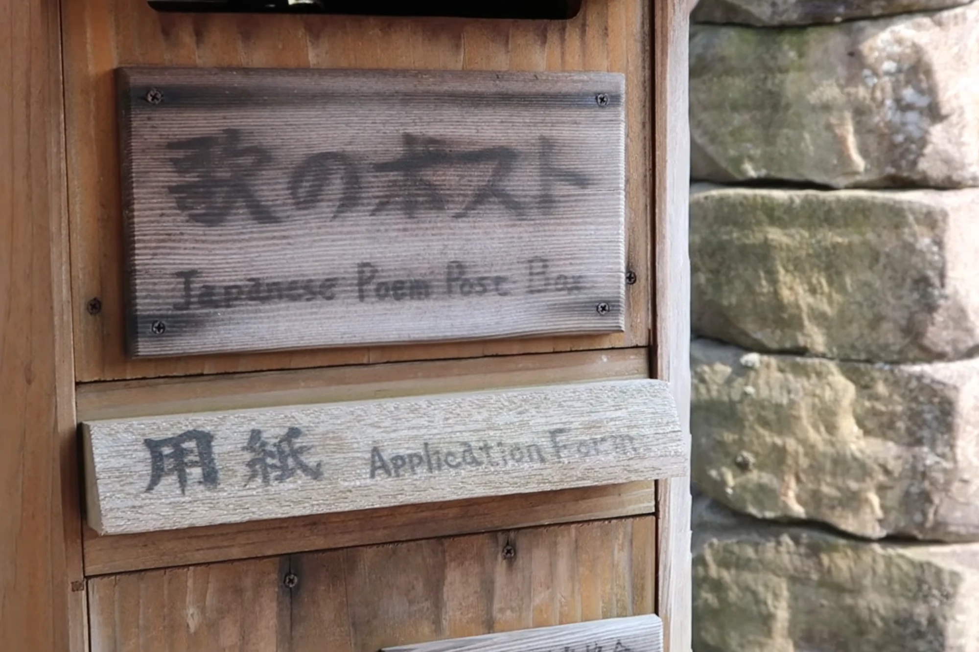 A weathered timber post box on a Kinosaki street labelled Japanese Poem Post Box.