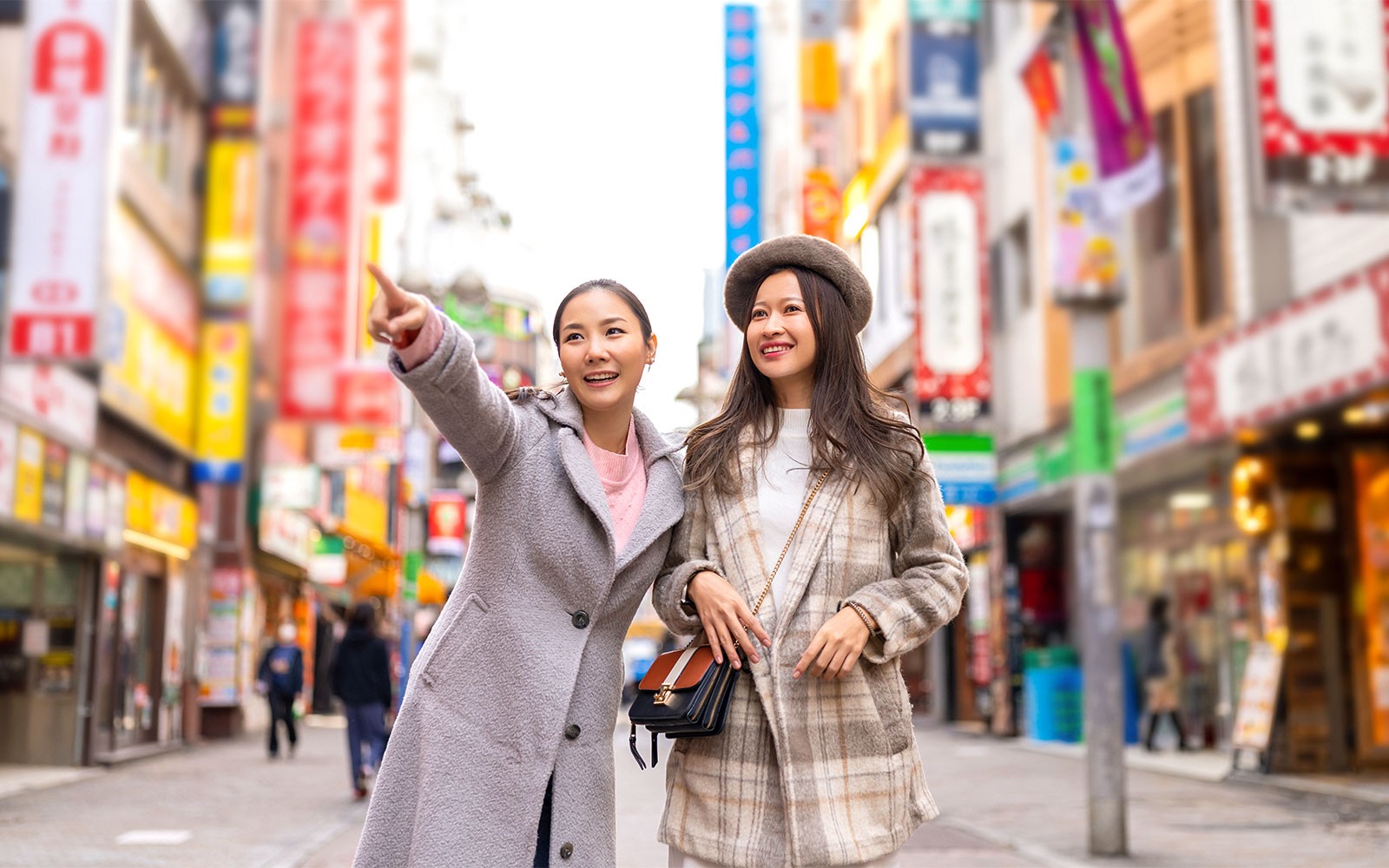 붐비는 인파와 도시의 불빛으로 둘러싸인 도쿄 시부야 횡단보도에서 포즈를 취하는 두 여성.