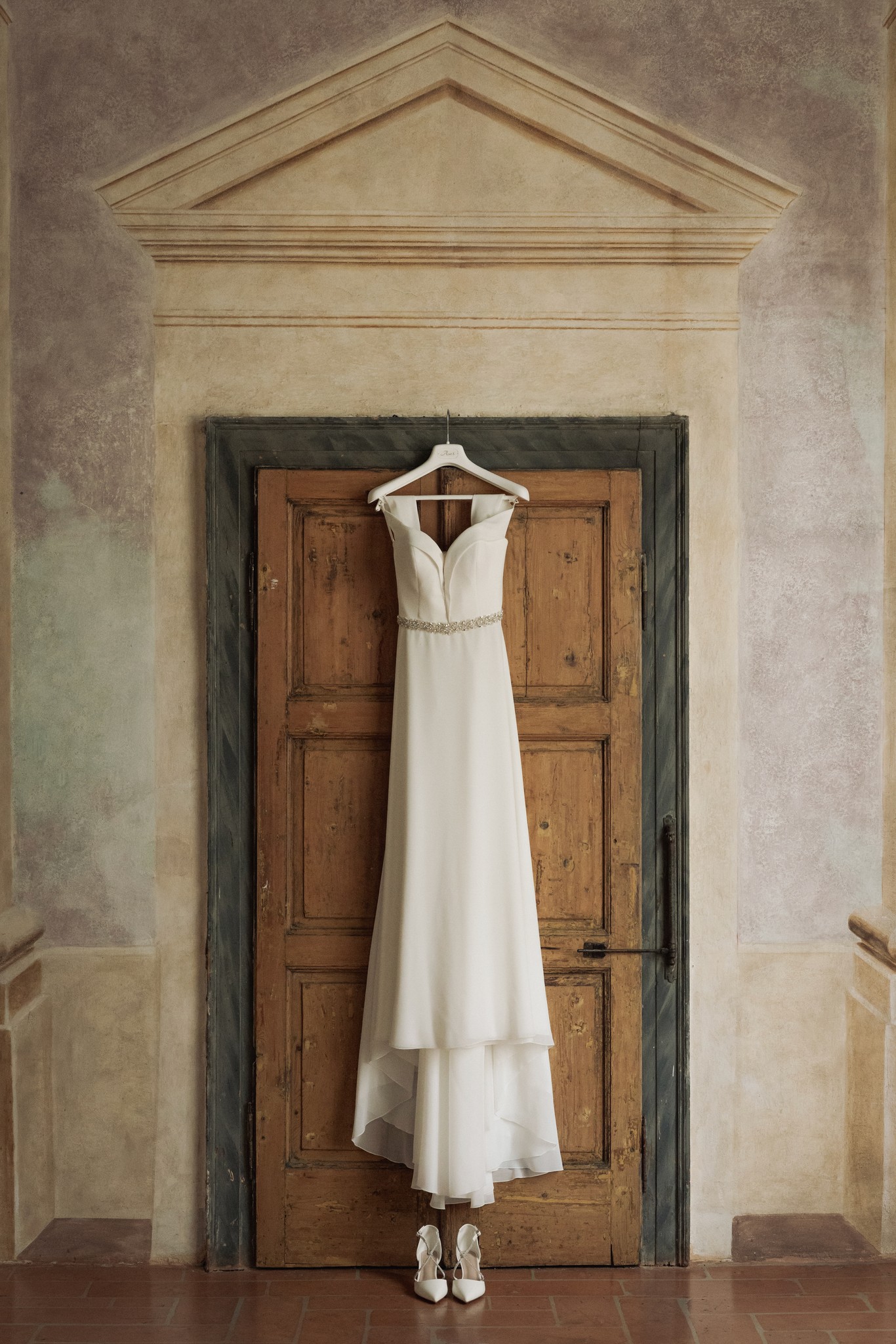 Abito bianco da sposa su gruccia davanti a porta in legno scuro, preparativi matrimonio a Villa Negri