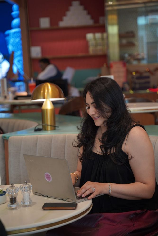 Karishma smiling as she works on her laptop in a café