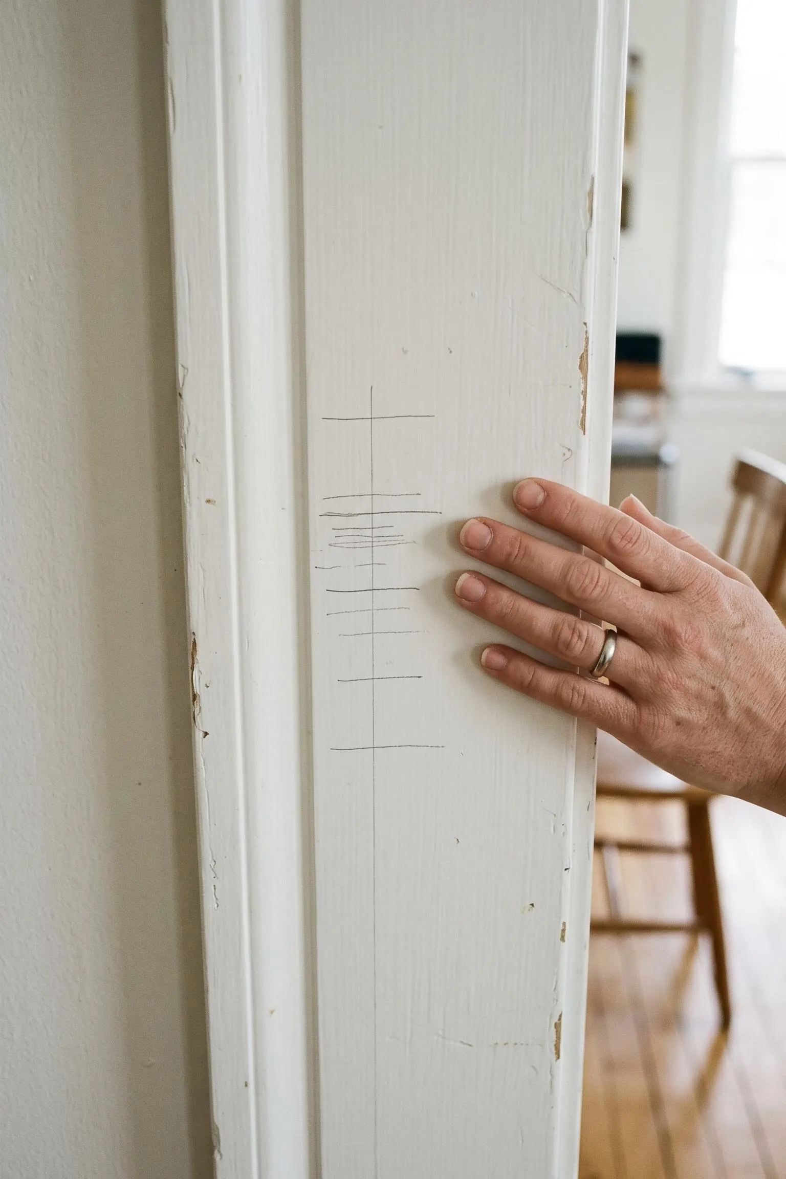 Pencil height marks on a painted doorframe in an old house, a hand resting beside them
