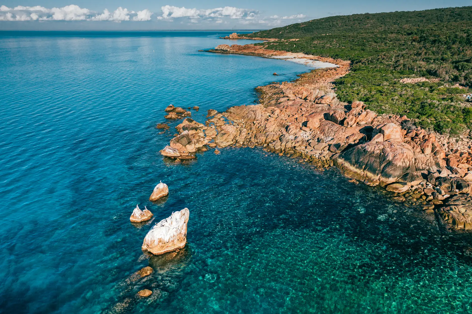 Aerial of a rocky point with granite outcrops in clear blue water