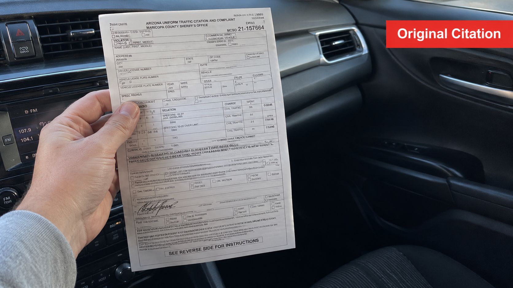 A person holding an Arizona Uniform Traffic Citation and Complaint document inside a vehicle.