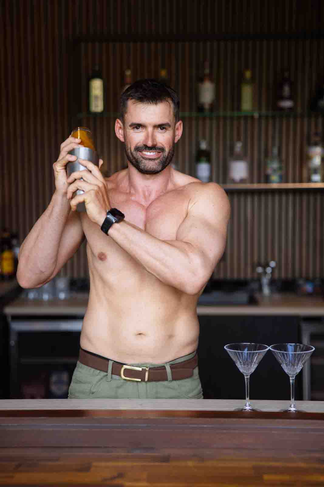 Shirtless man shaking cocktail in bar