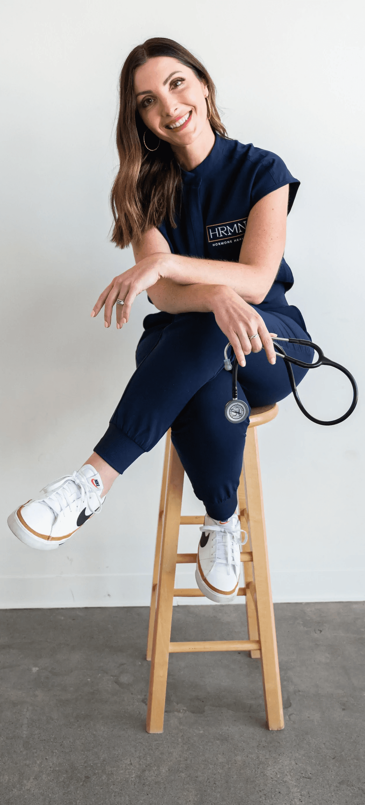 Portrait of Jamie Ruiz, a certified Physician Associate, smiling in a professional medical setting with shelves of supplements and medical products in the background.
