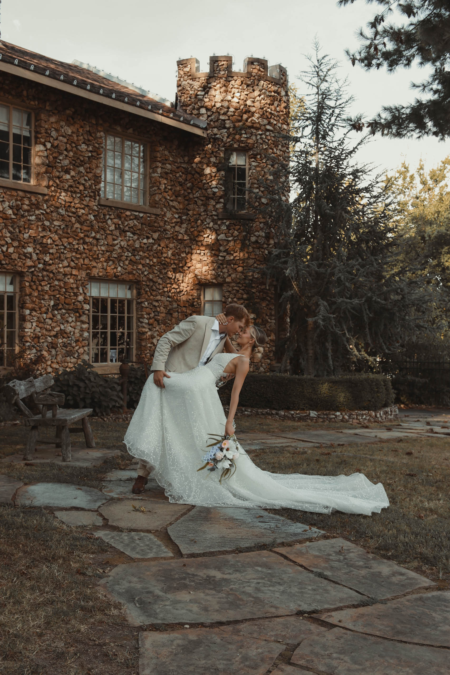 Bride and groom doing a dip and kissing in front of a castle.