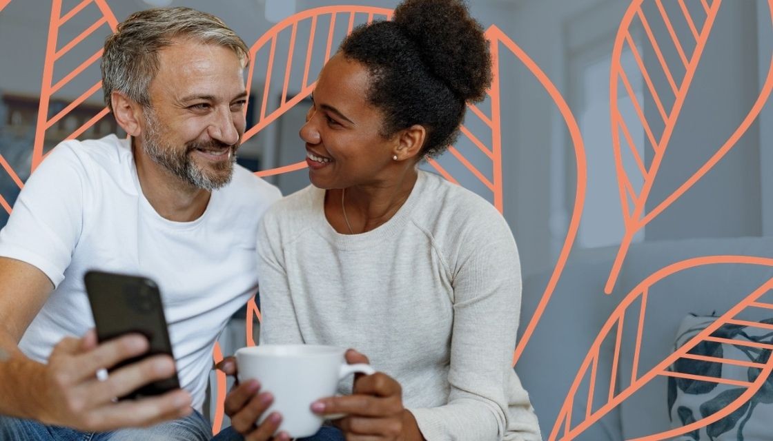 A couple smiling at each other looking at a cell phone