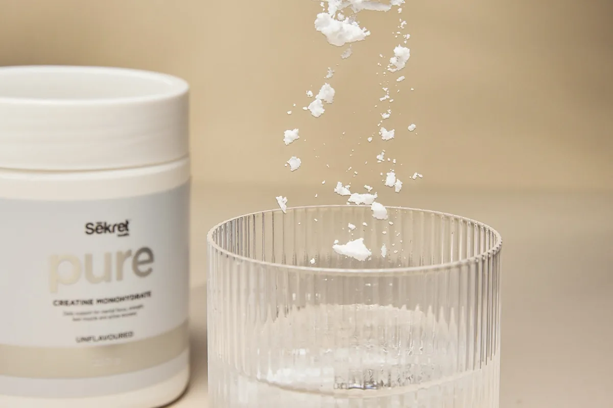 Sēkret Pure creatine poured into a glass of water beside the tub
