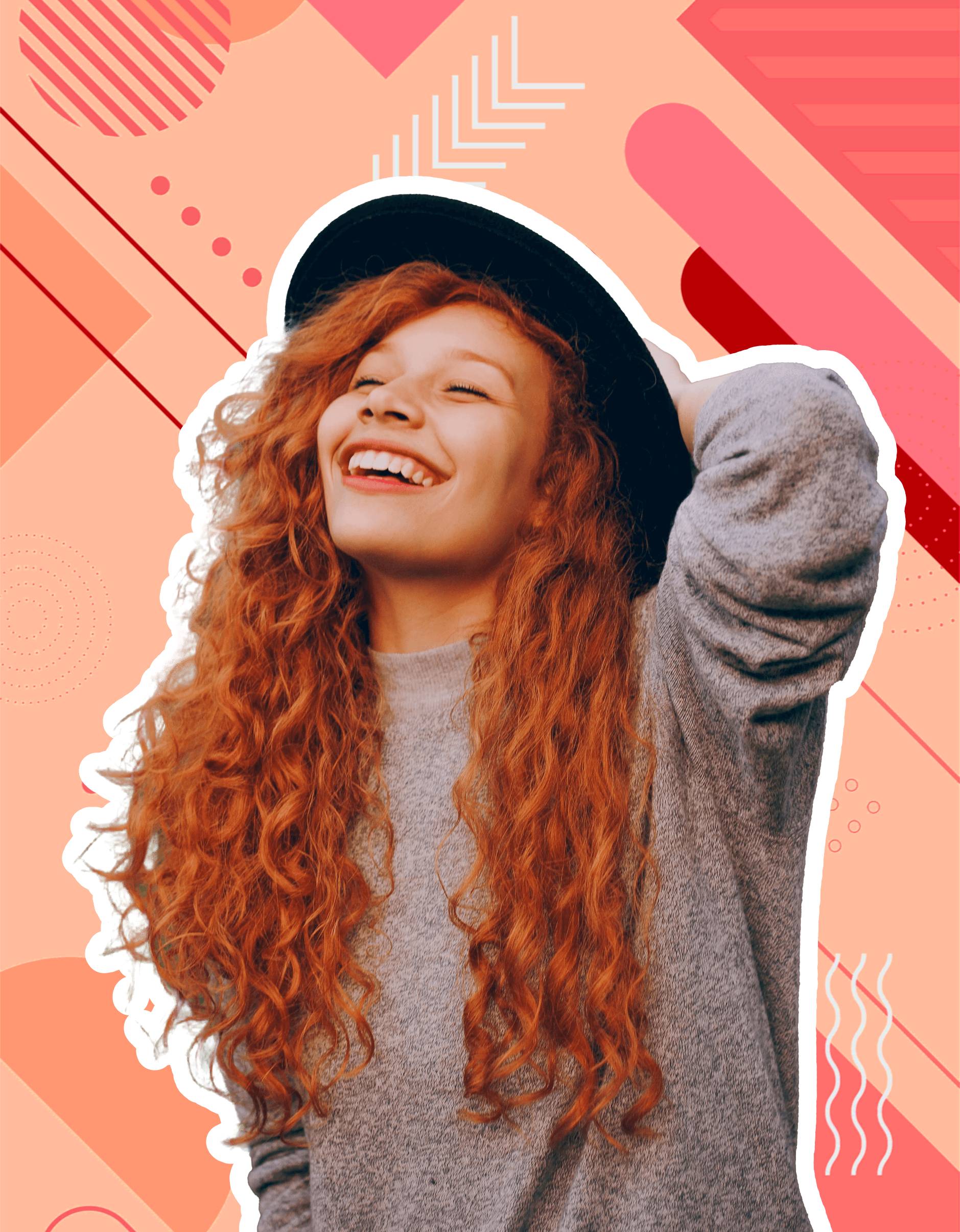 A woman with curly red hair and a black hat smiles, holding her hair back.