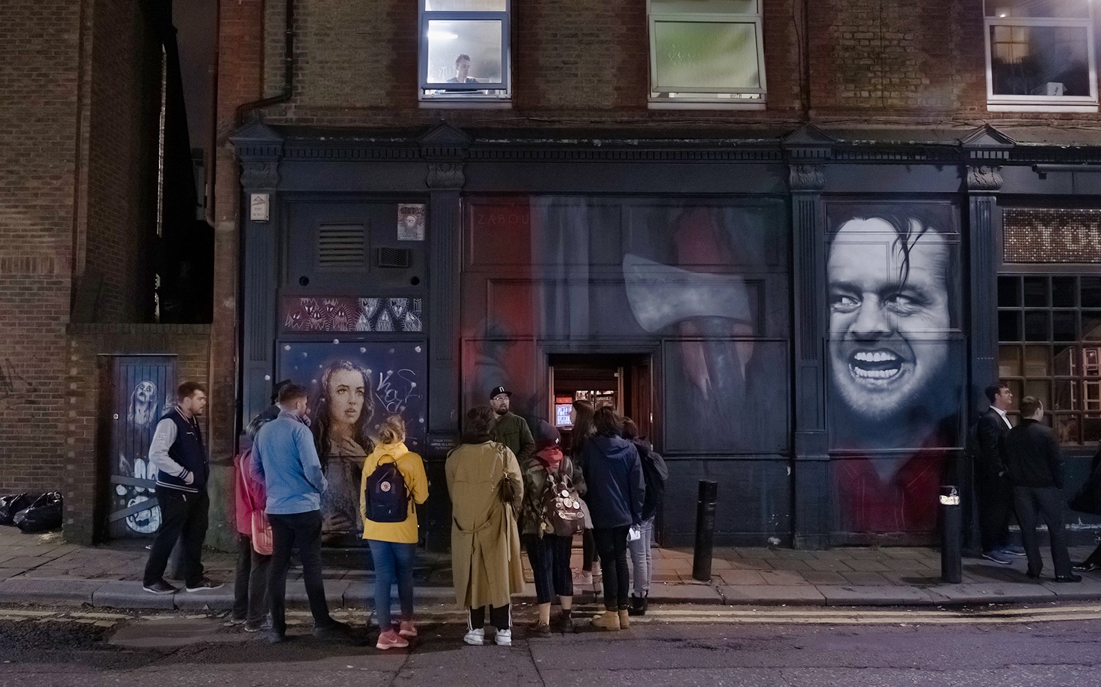 Group of people on a Jack the Ripper tour outside a mural-covered building in London.
