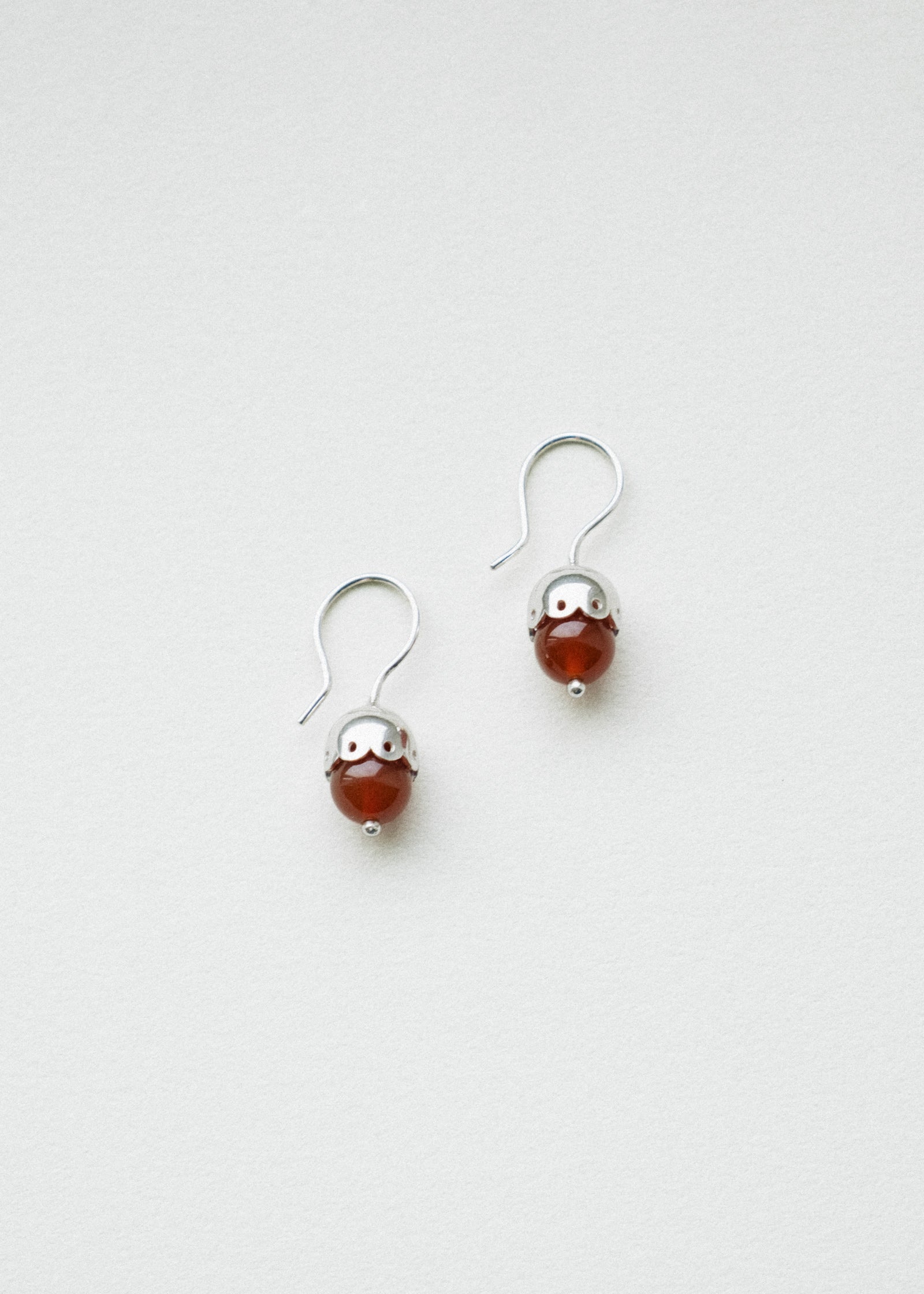 Pair of silver earrings with red carnelian beads on a white background