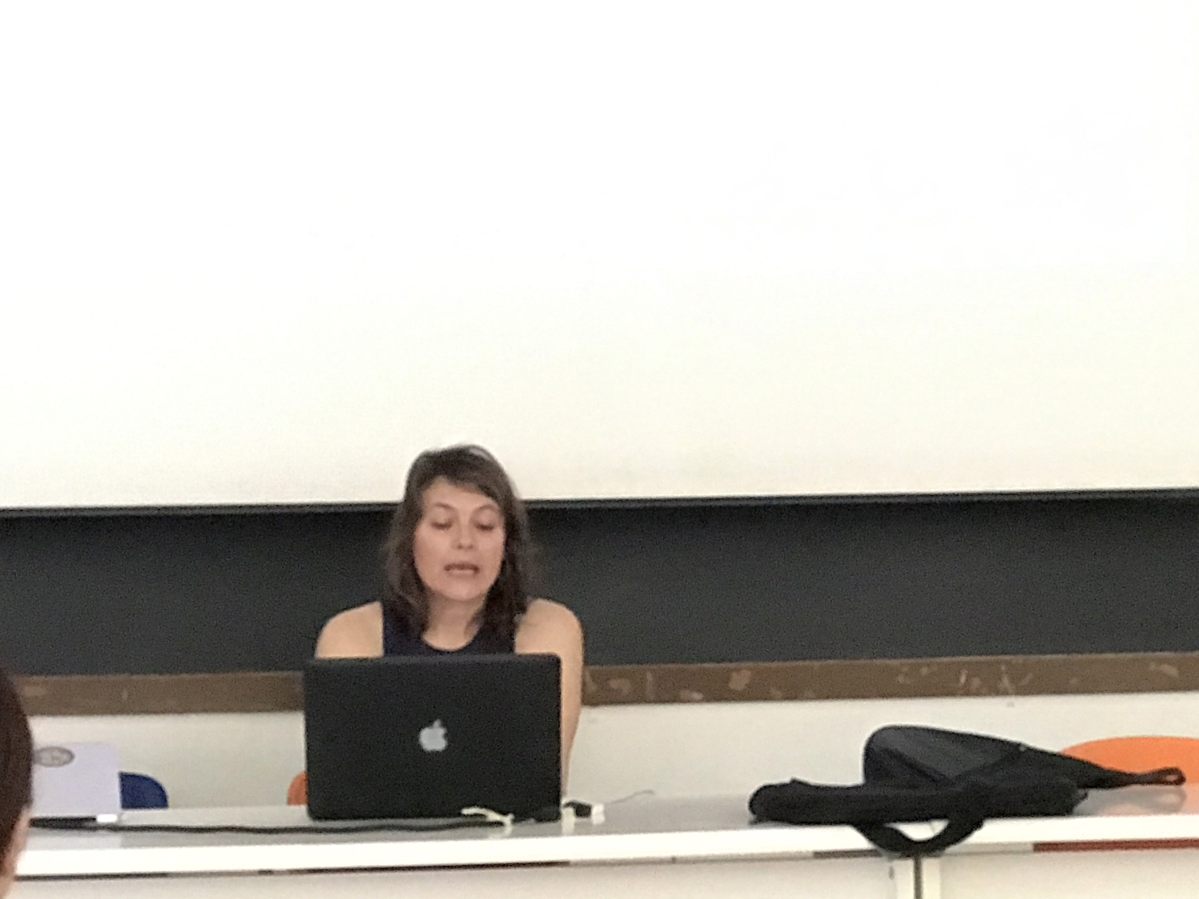 A photography showing a women speaking while looking at a laptop.