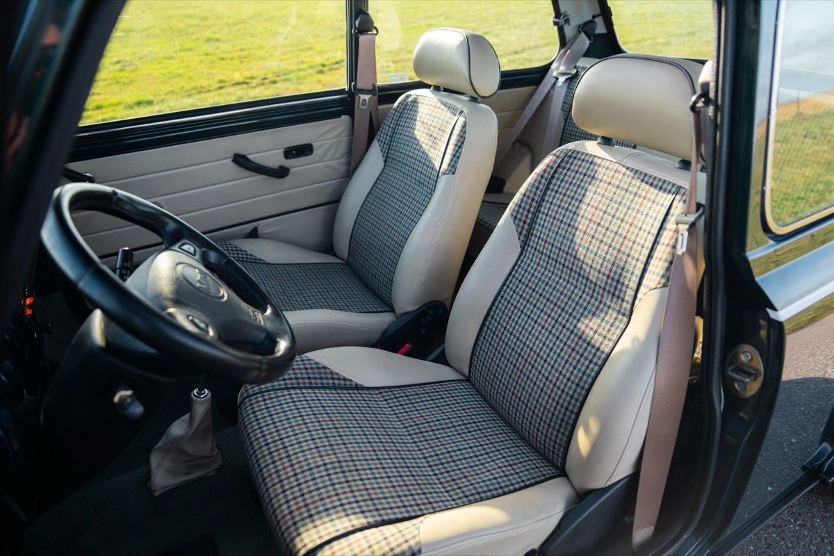 Interior of a car showing two front seats with gray fabric upholstery and a steering wheel. Green field outside.