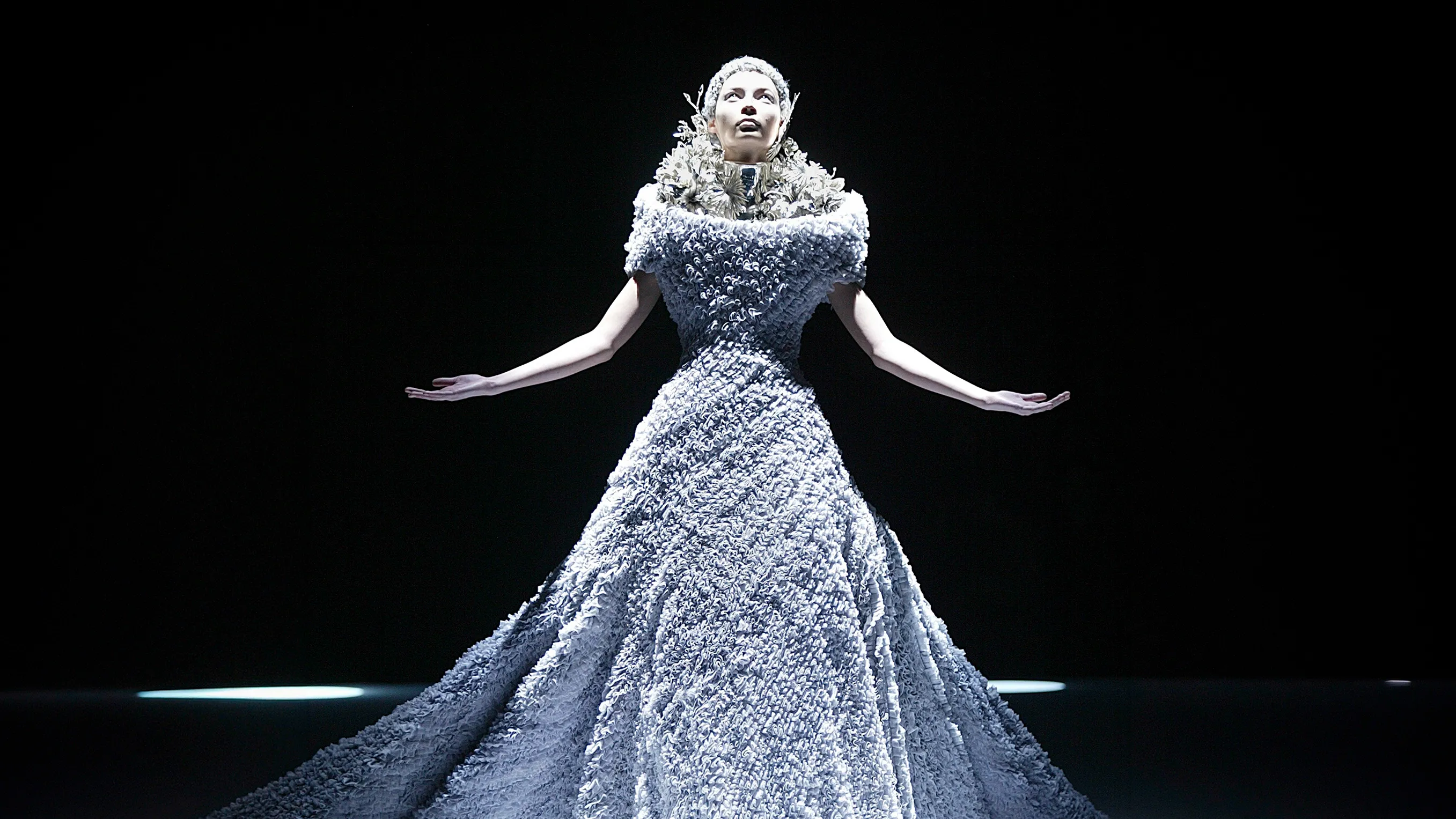 Dramatic runway shot of a model looking upward in a textured, voluminous ballgown paired with the silver metal Rose Corset neckpiece and matching floral headpiece, designed by Shaun Leane for Alexander McQueen's "The Widows of Culloden" Autumn/Winter 2006 collection.