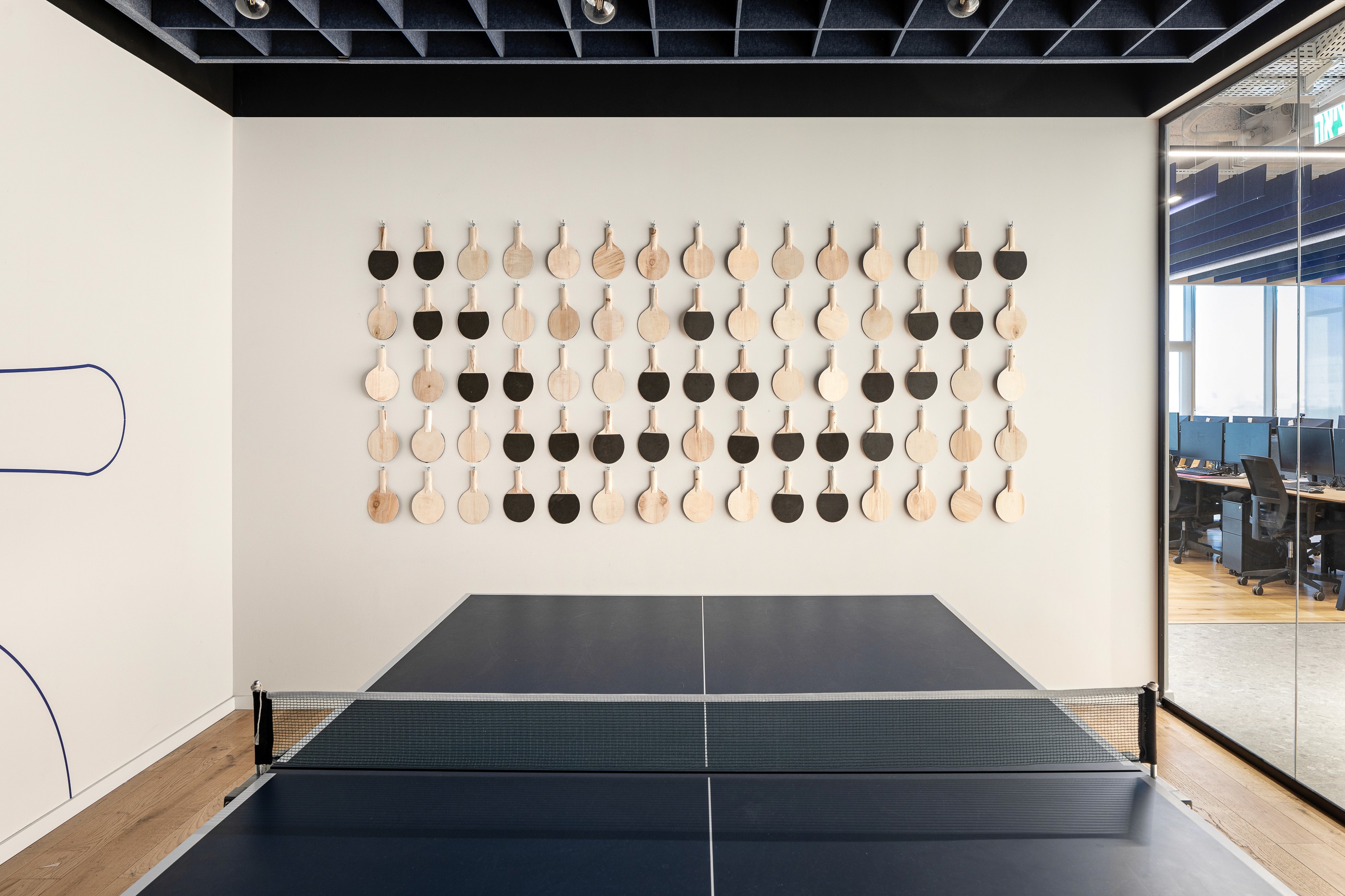 קיר דקורטיבי בחדר המשחקים: מיצב אומנותי המורכב ממטקות פינג-פונג תלויות, המתכתב עם שולחן המשחק ומוסיף הומור ואופי ייחודי לחלל.