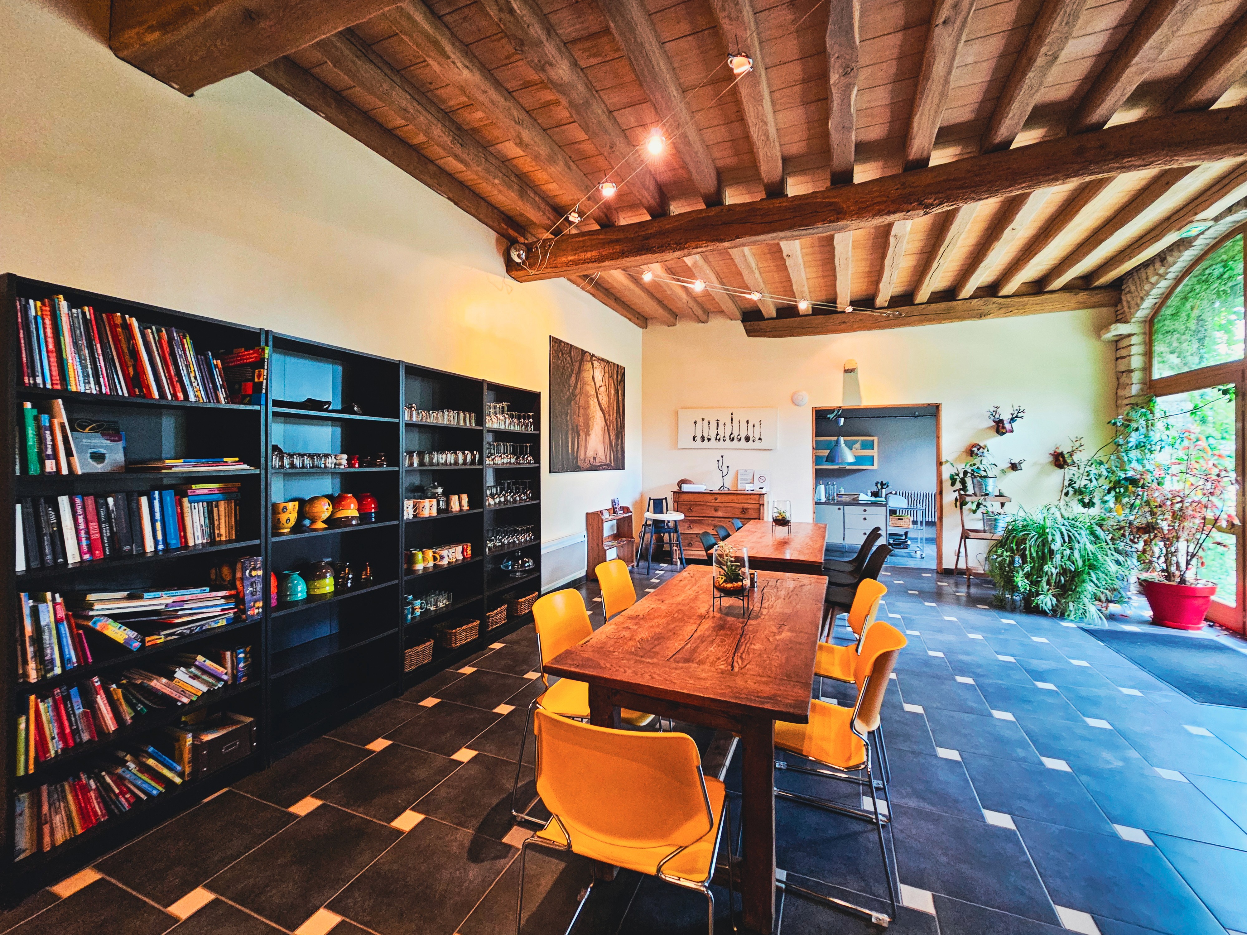 Salle à manger rustique avec grande table en bois, étagères, livres et vaisselle
