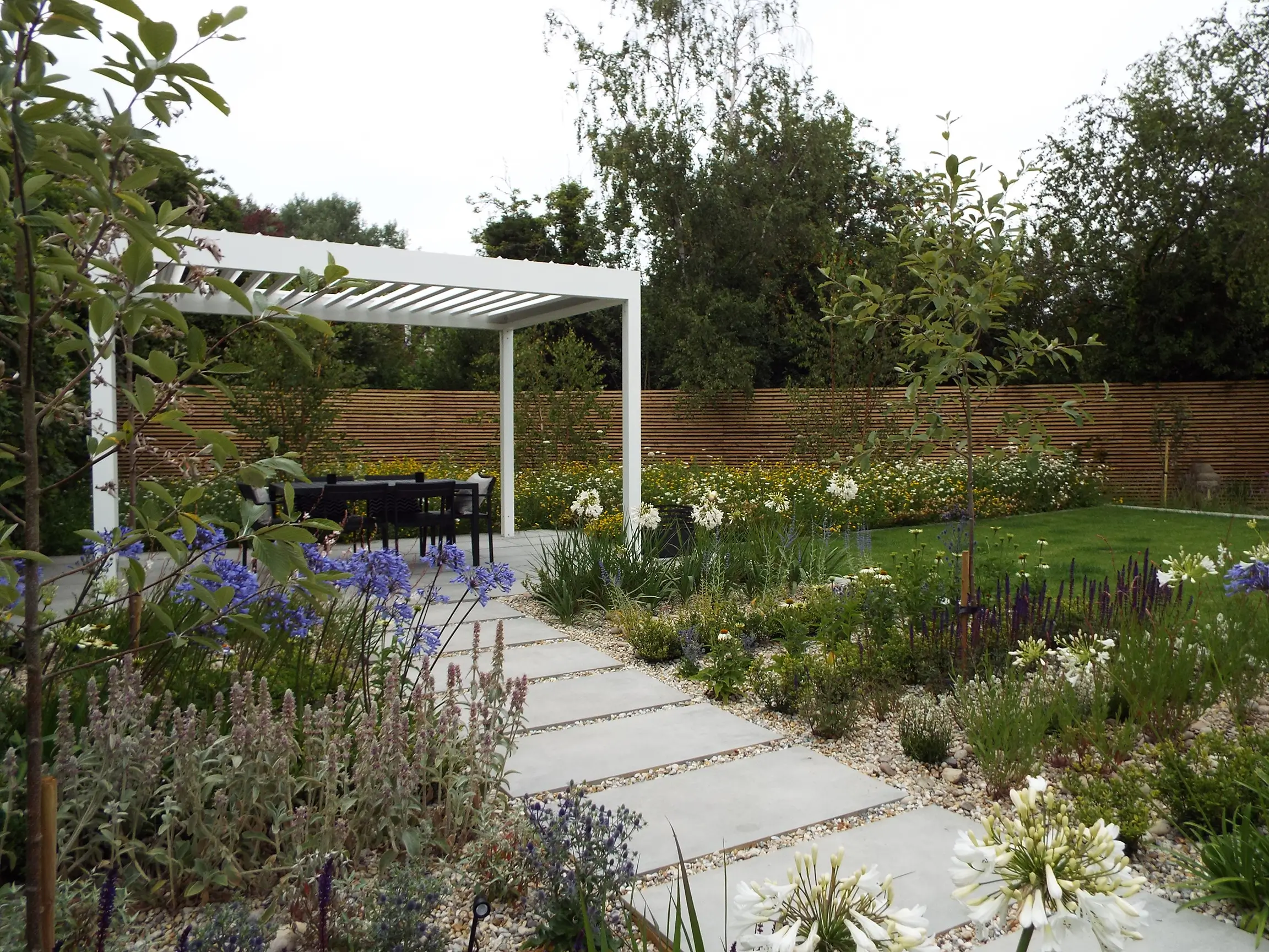 A serene garden pathway leads to a wooden pergola surrounded by greenery and plants.