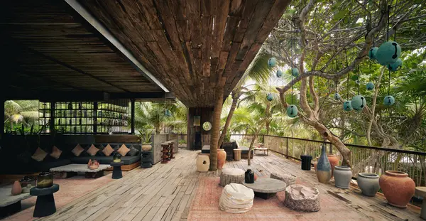 Sky Terrace restaurant at Be Tulum: covered terrace surrounded by seating options like poufs, sofas, and center tables for dining and drinking, amidst trees and selvatic zone.