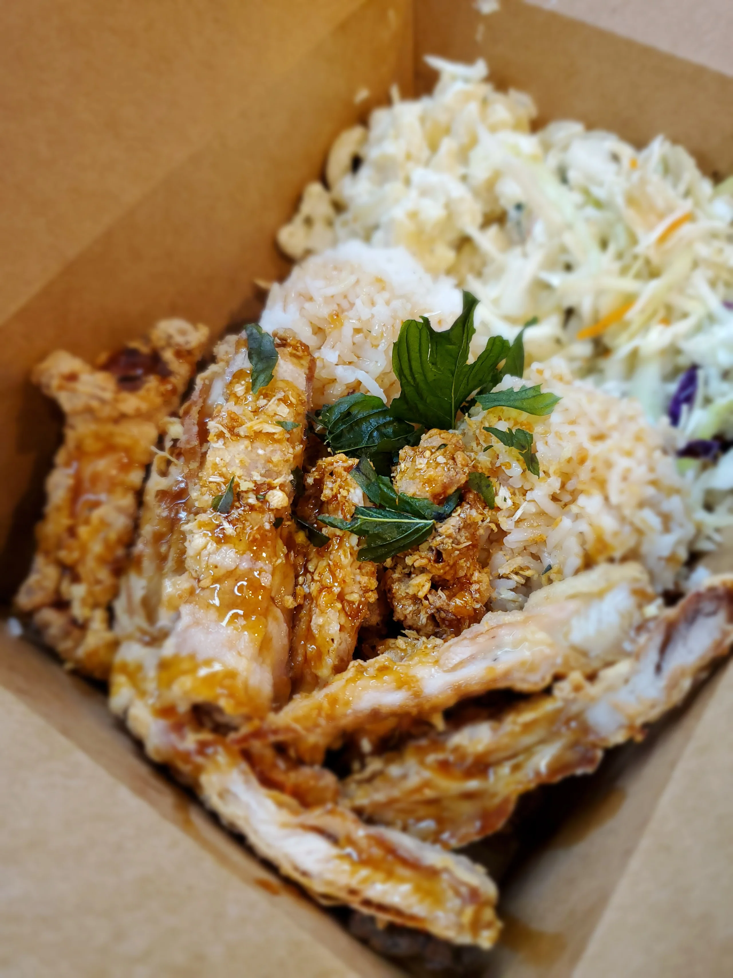 Crispy mochiko fried chicken topped with green fried basil leaves and golden garlic, drizzled with tamarind glaze in a bowl with rice and sides.