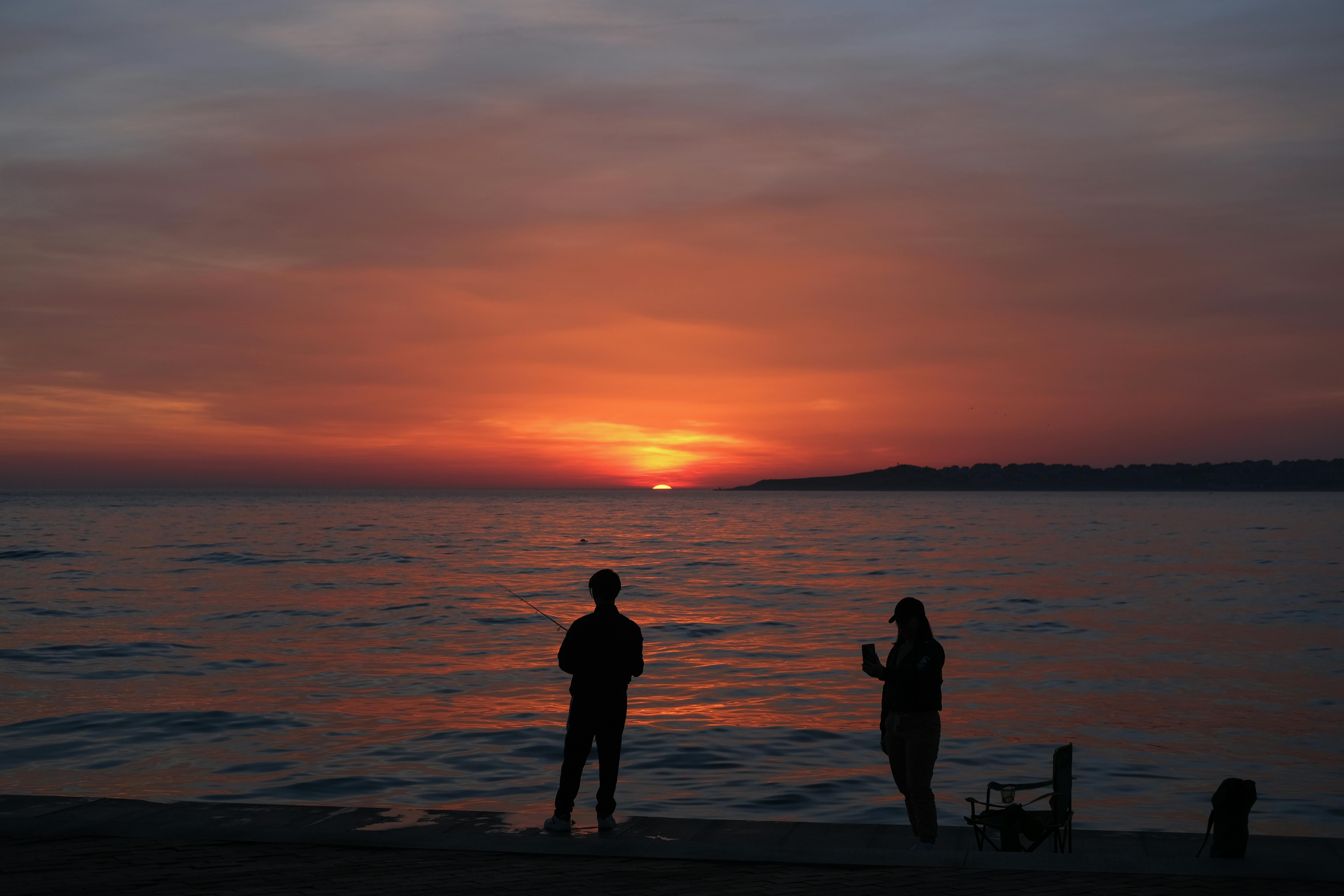 Silhouettes of two people against a vibrant sunset over the water, creating a serene and peaceful atmosphere.