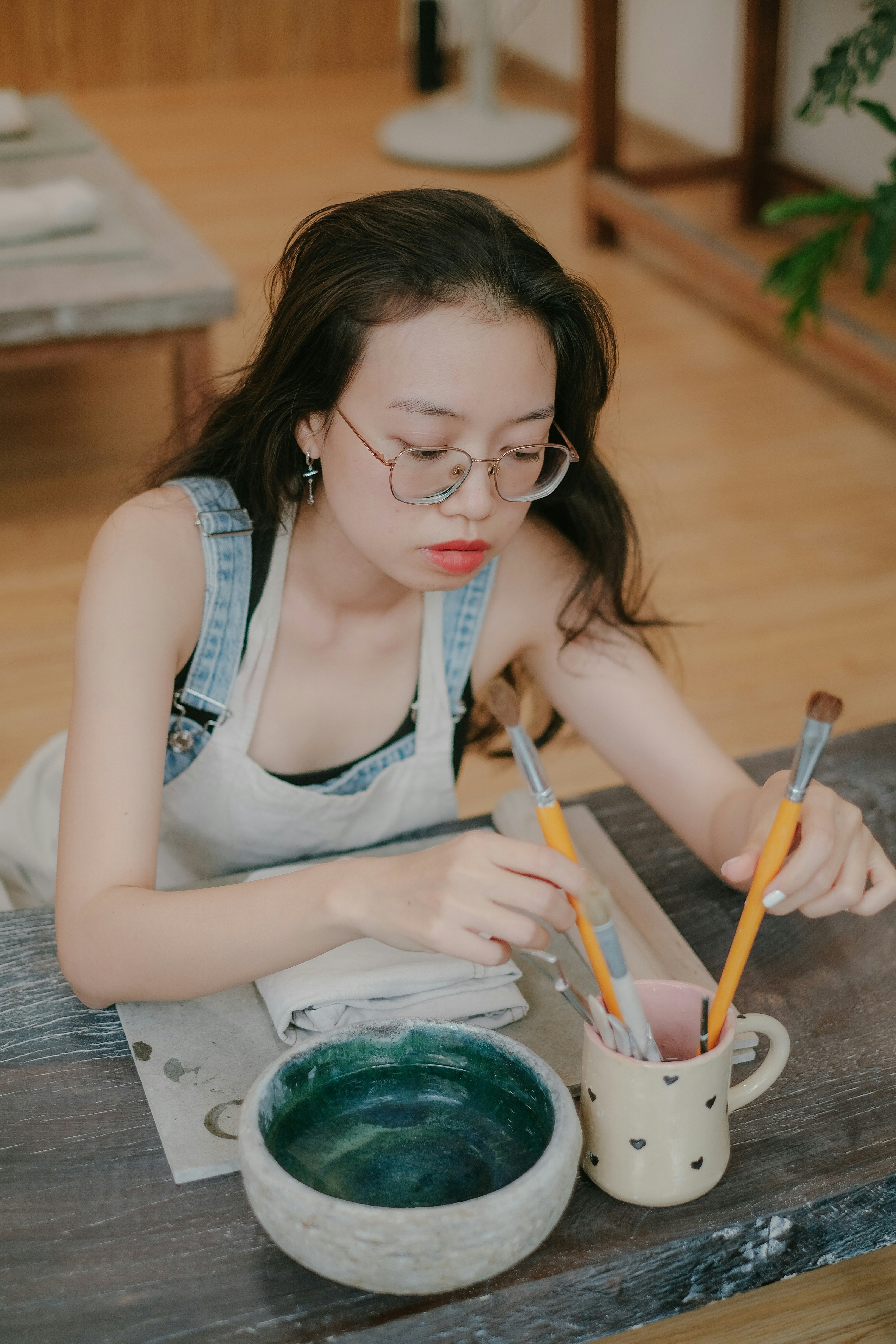 a woman sitting at a table with a bowl of green liquid and two pencils